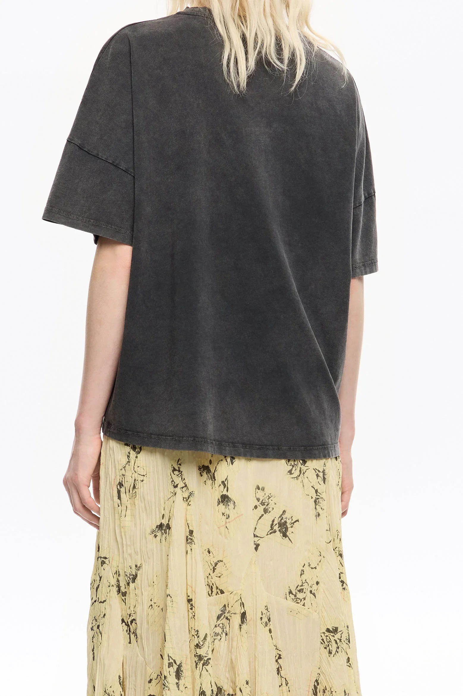 אישה לובשת חולצת טי שחורה בסגנון אוברסייז וחצאית פליסה בהירה עם הדפס פרחוני, אופנת CHOZEN