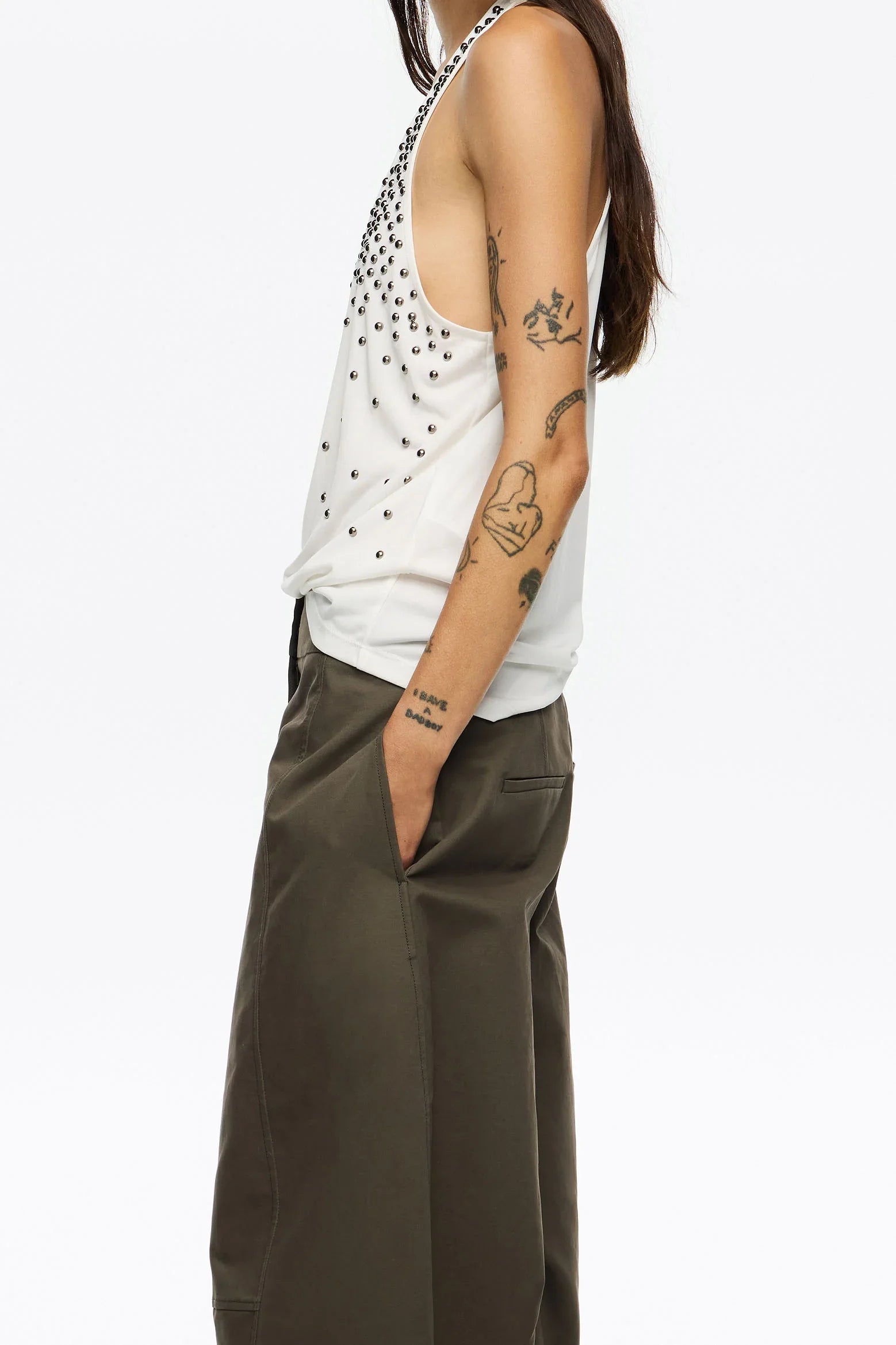 דוגמן לובש גופיית נשים לבנה עם ניטים ומכנסיים ירוקים, טאטואים בולטים, צילום אופנה ל-CHOZEN