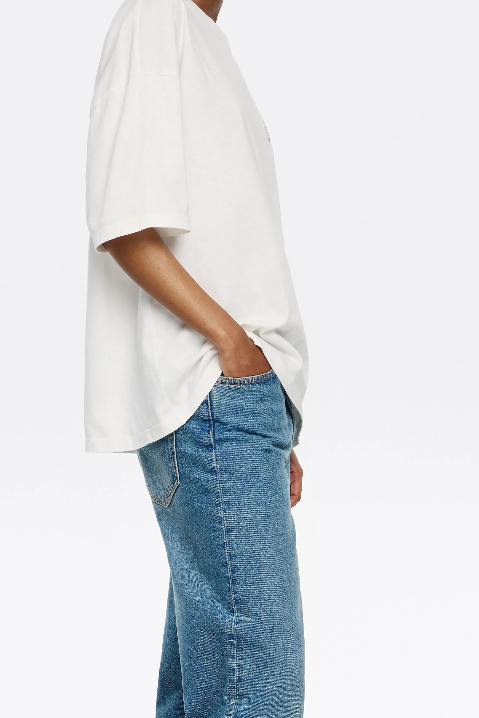 אדם לובש חולצת טי לבנה ומכנסי ג'ינס כחולים, צילום צד לאתר CHOZEN מבית קבוצת אלפא