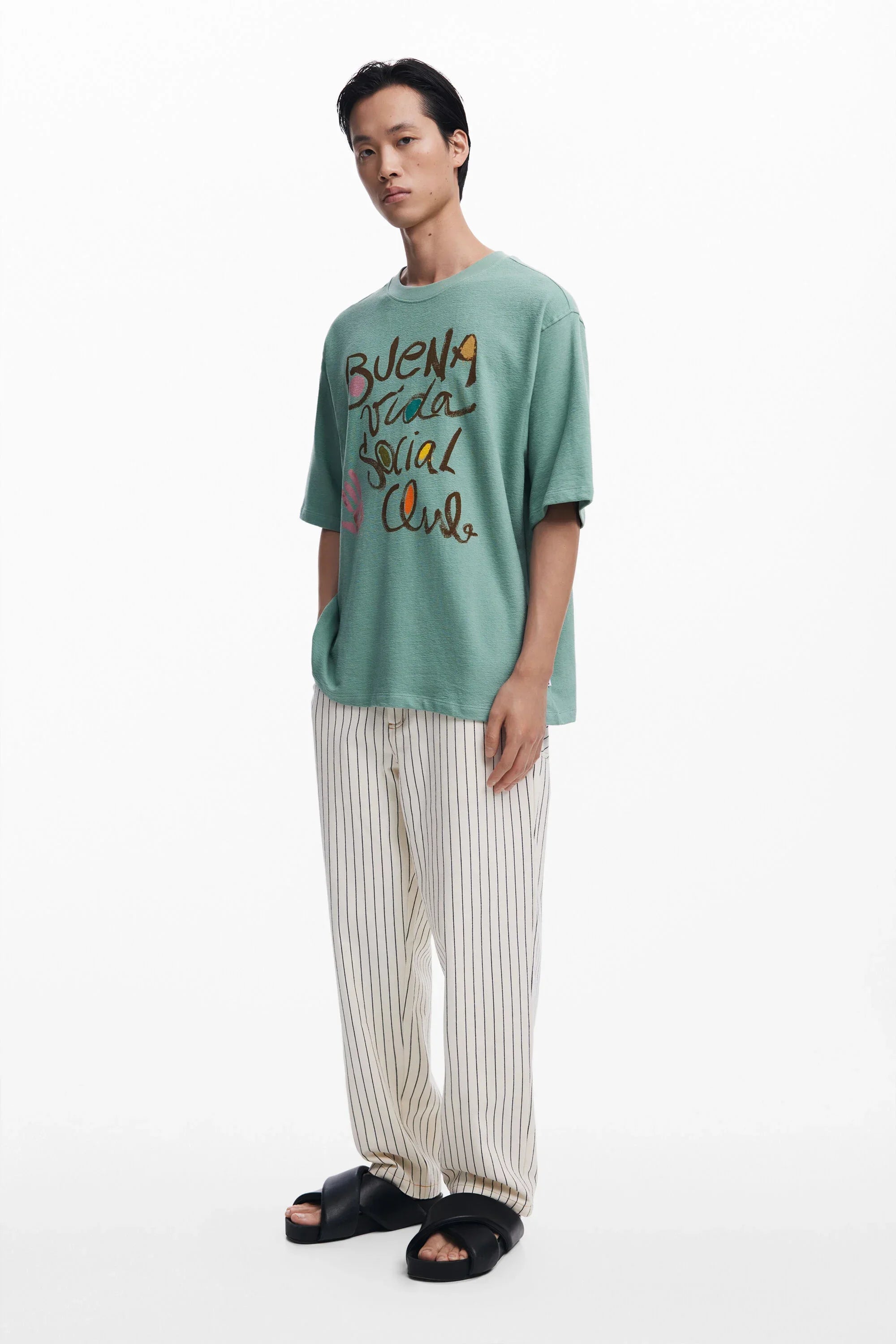 גבר לובש חולצת טי ירוקה עם כיתוב צבעוני ומכנסי פסים לבנים, אופנת CHOZEN קבוצת אלפא