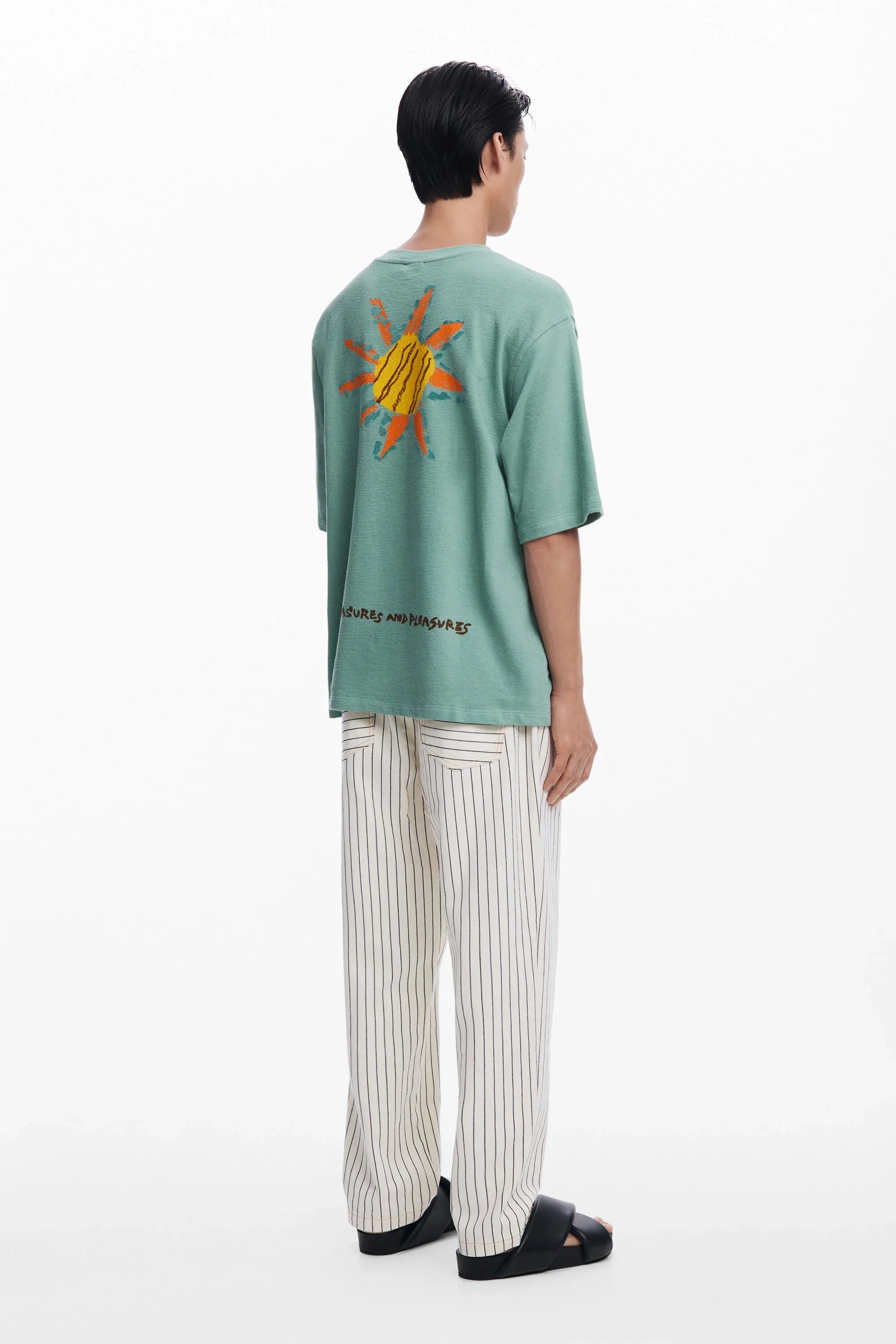 דוגמן לובש חולצה ירוקה עם הדפס שמש צבעוני מאחור, מכנס פסים ונעלי סלייד CHOZEN