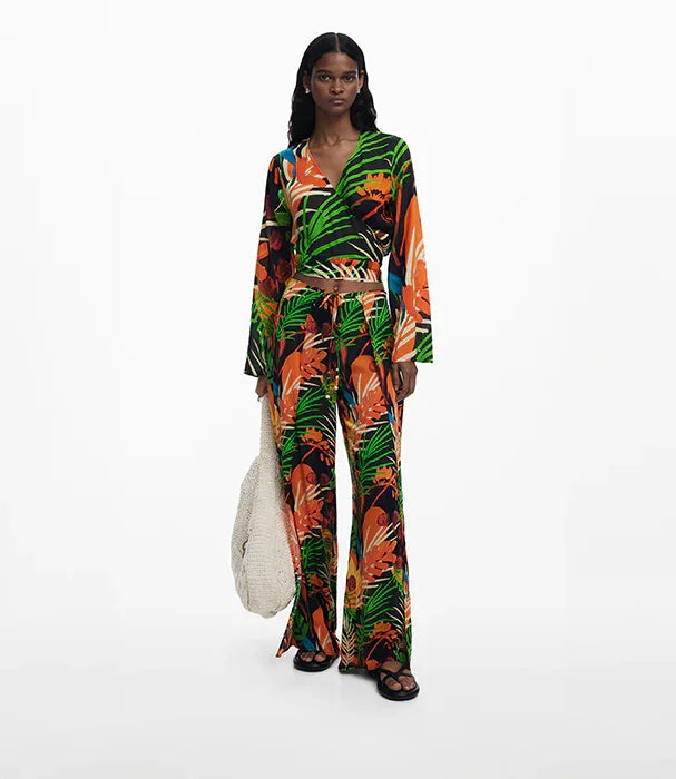אישה לובשת חליפת טרופית צבעונית עם הדפס עלים, נעלי קיץ ותיק קלוע, צילום לאופנה CHOZEN