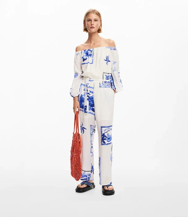 אישה לובשת אוברול לבן עם הדפסים כחולים, תיק כתום וסנדלים שחורים, צילום אופנה CHOZEN