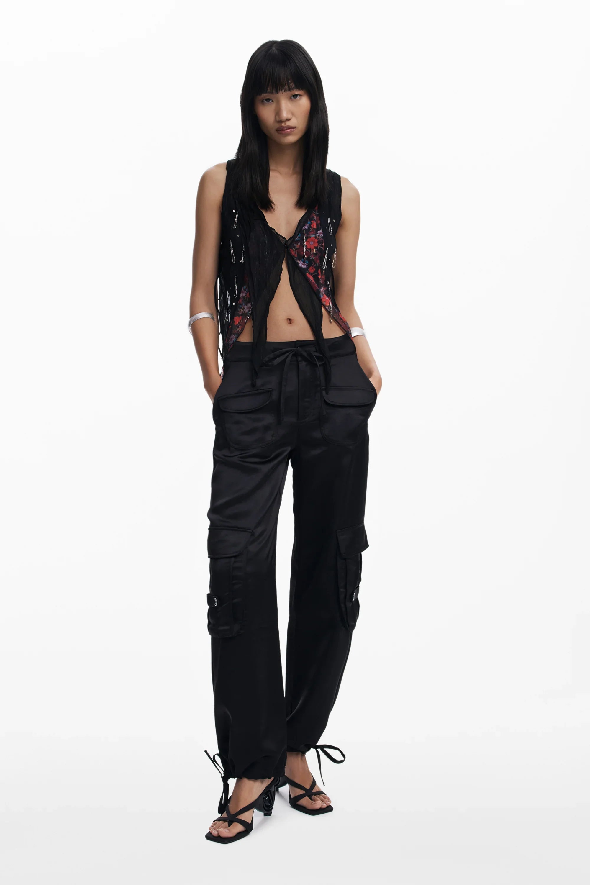 אישה לובשת מכנסי קרגו שחורים עם כיסים, חולצה קצרה פתוחה ונעלי עקב שחורות