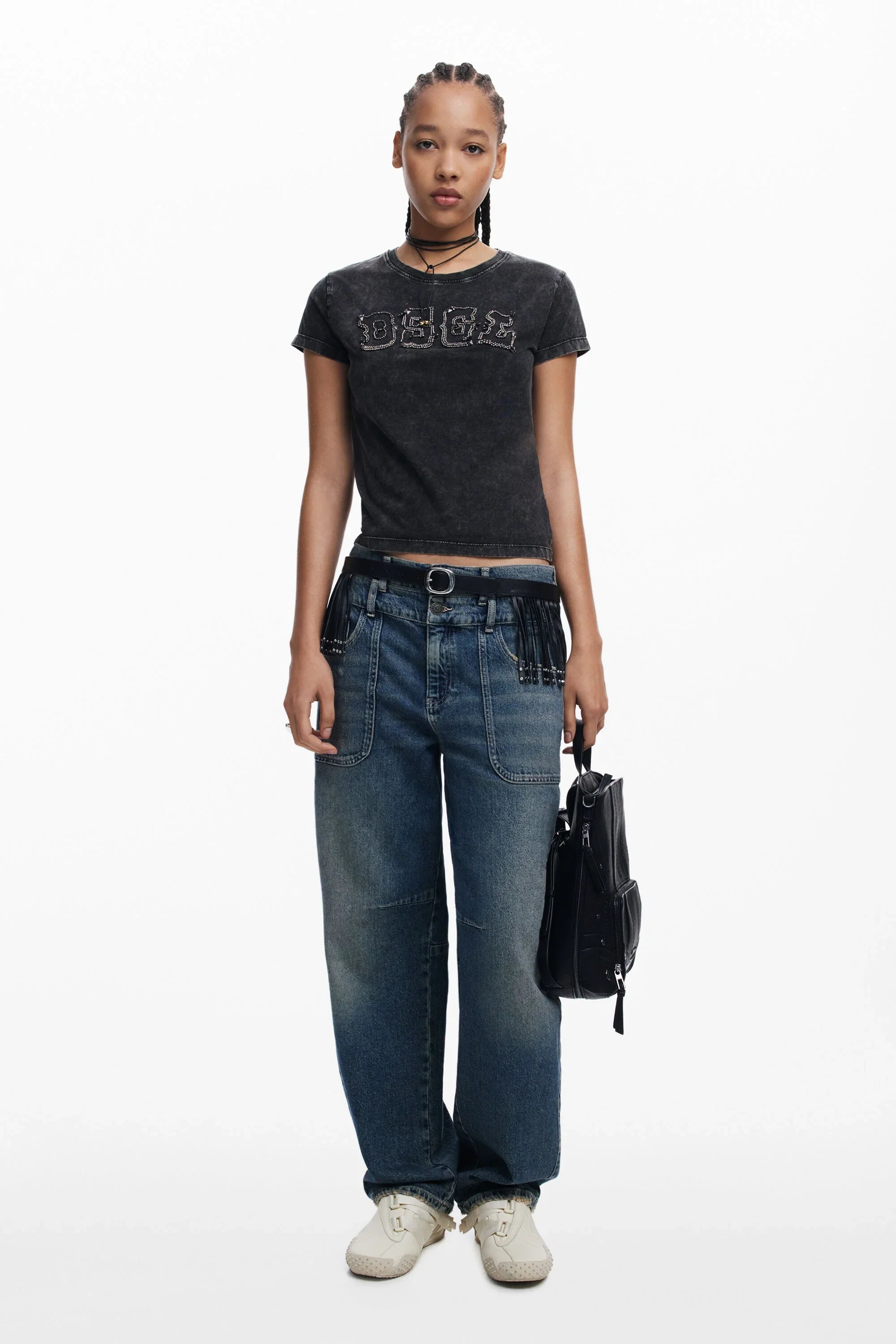 דוגמנית לובשת חולצת טי שחורה עם כיתוב, ג'ינס רחב ונעליים לבנות, מחזיקה תיק צד. אופנה עכשווית CHOZEN