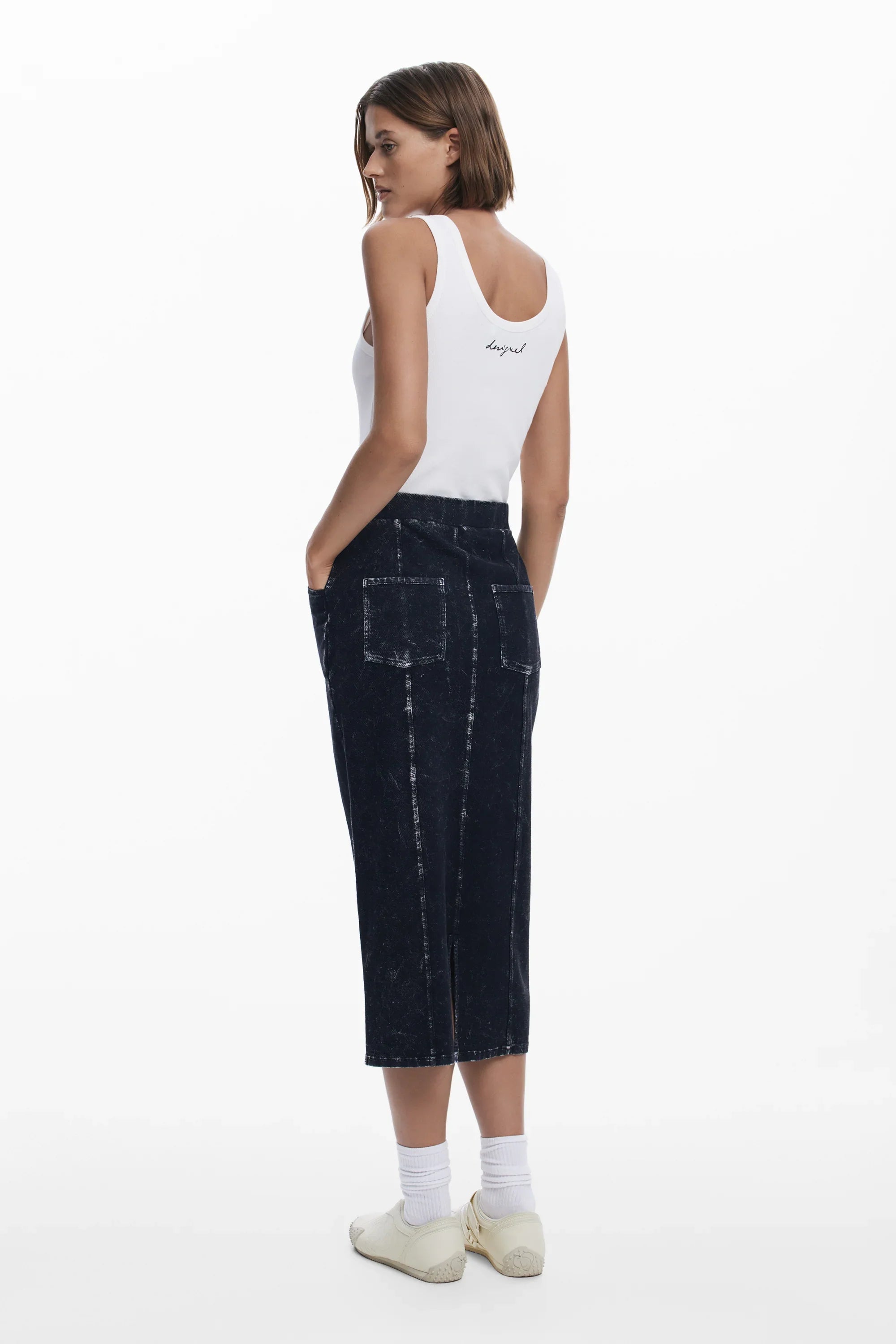 דוגמנית לובשת גופיה לבנה עם הדפס גב, חצאית ג'ינס כהה, נעלי סניקרס לבנות, צילום לאופנה מבית CHOZEN