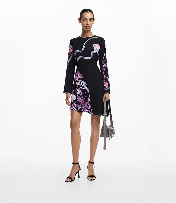 אישה לובשת שמלת מיני שחורה עם דוגמת ורוד וסגול, נעליים פתוחות, תיק כסוף, CHOZEN אופנה יוקרתית