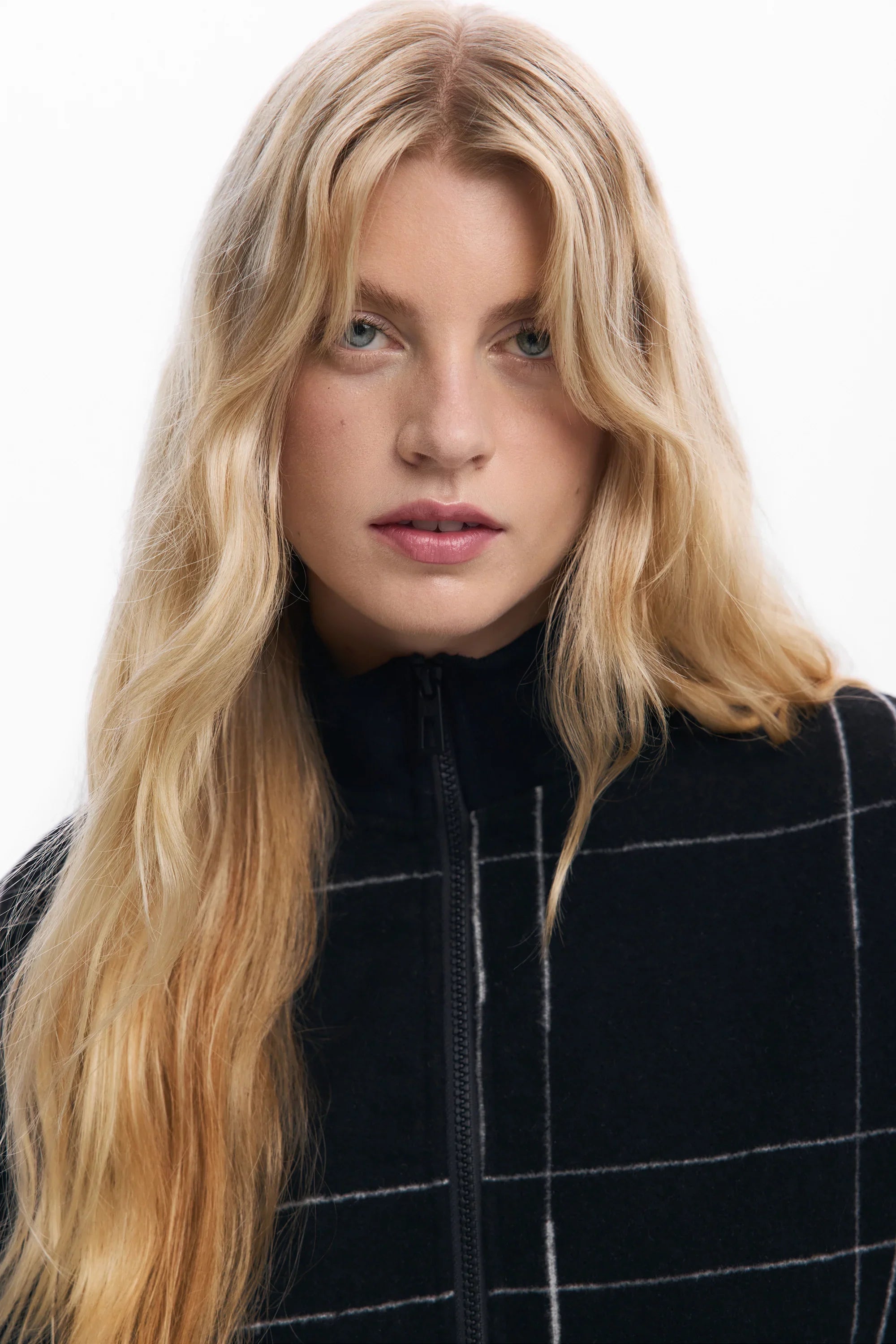 אישה עם שיער בלונדיני ארוך ולבושה ג'קט משובץ שחור-לבן, אופנה CHOZEN