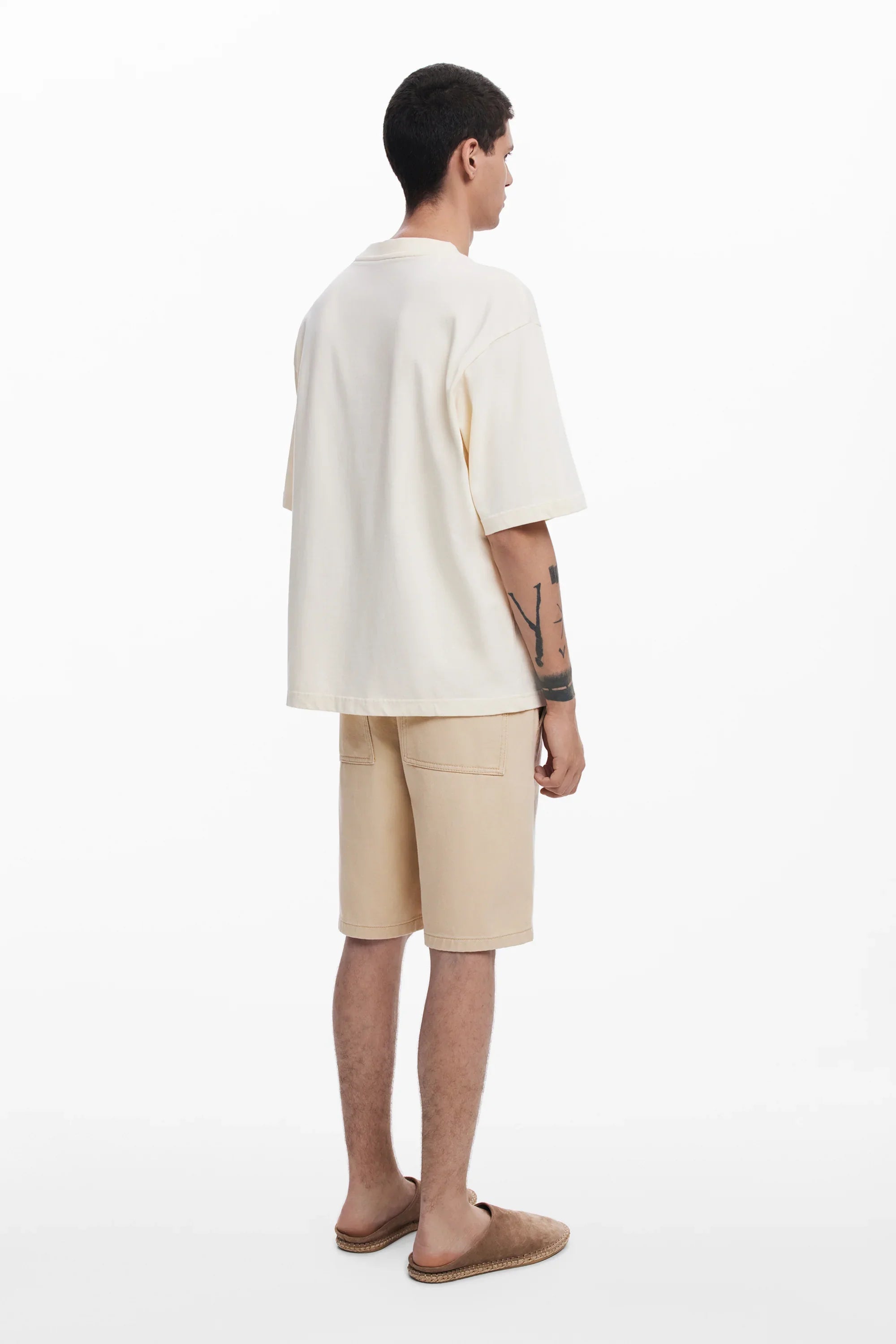 גבר לובש חולצת טי שירט בהירה ומכנסיים קצרים בז' מבית CHOZEN, צילום על רקע לבן