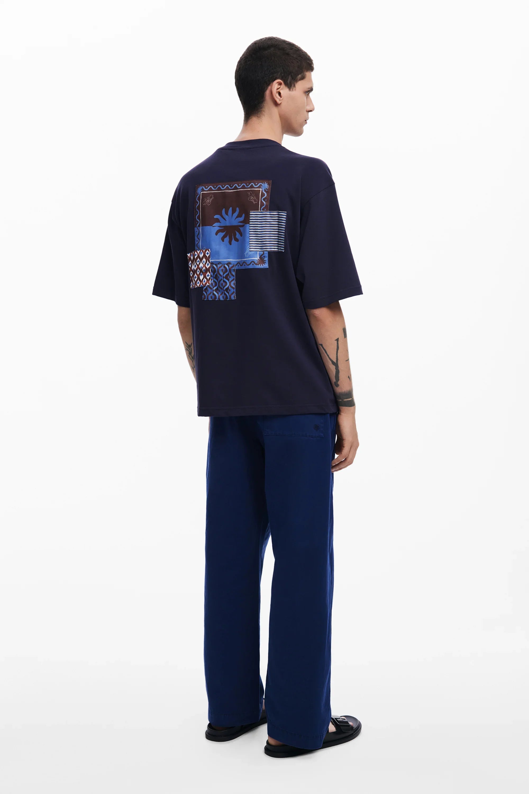 דוגמן לובש חולצת טי כהה עם הדפס גיאומטרי כחול ומכנסיים כחולים, צילום אופנה ל-CHOZEN