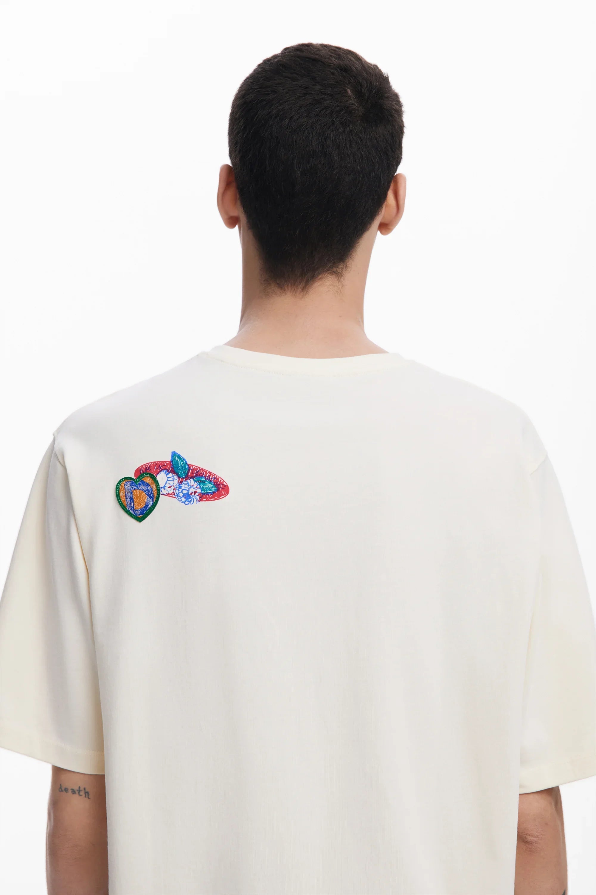 חולצת טי שירט לבנה של CHOZEN עם דוגמת רקמה צבעונית בגב, צילום מהצד האחורי
