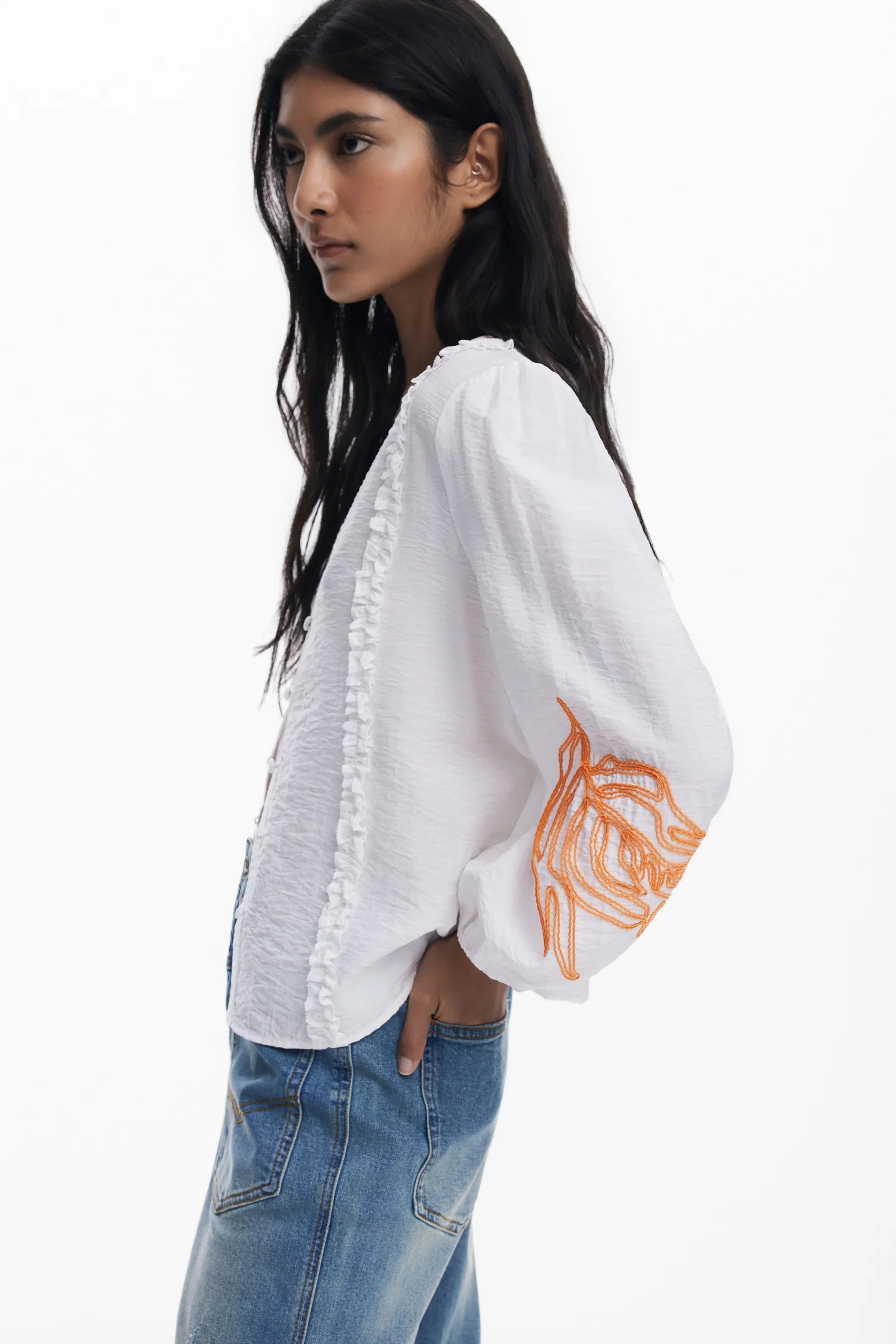 דוגמנית לובשת חולצה לבנה עם רקמה כתומה על השרוול וג׳ינס, אופנה עדכנית CHOZEN