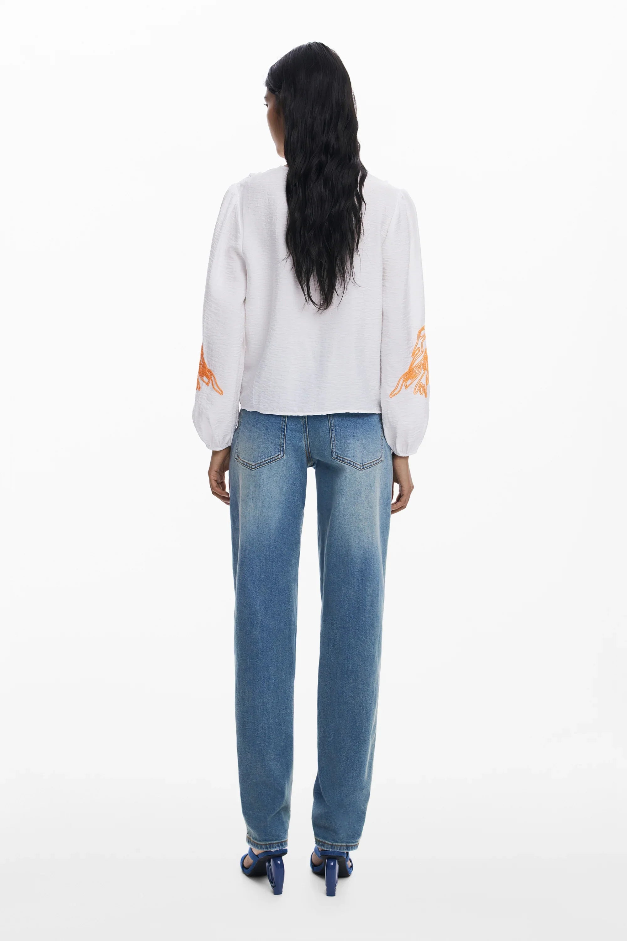 אישה עם חולצה לבנה בעיטור כתום ומכנסי ג'ינס ישרים, אופנת CHOZEN