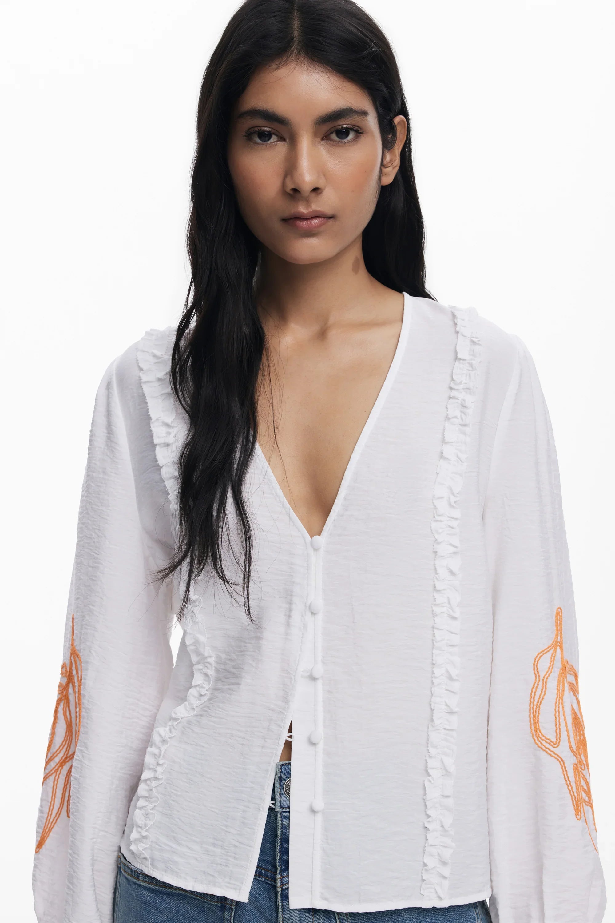 אישה לובשת חולצה לבנה עם כפתורים ועיטורי תפר כתומים בשרוולים, אופנה מבית CHOZEN
