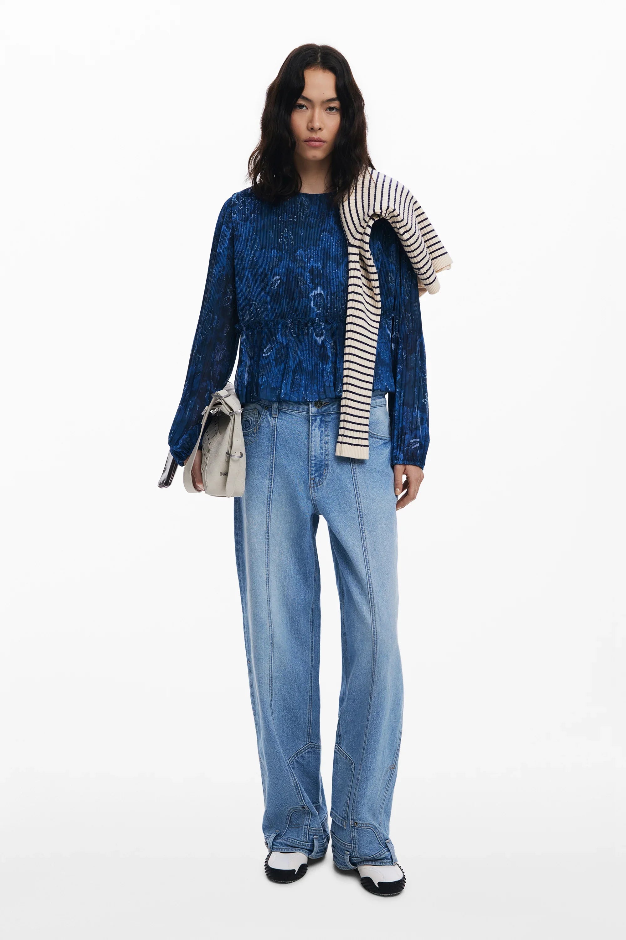 דוגמנית לובשת חולצה כחולה עם דוגמה וטקסטורה, מכנסי ג'ינס רחבים ונעליים לבנות שחורות, עם סוודר פסים על הכתף, אופנת נשים CHOZEN