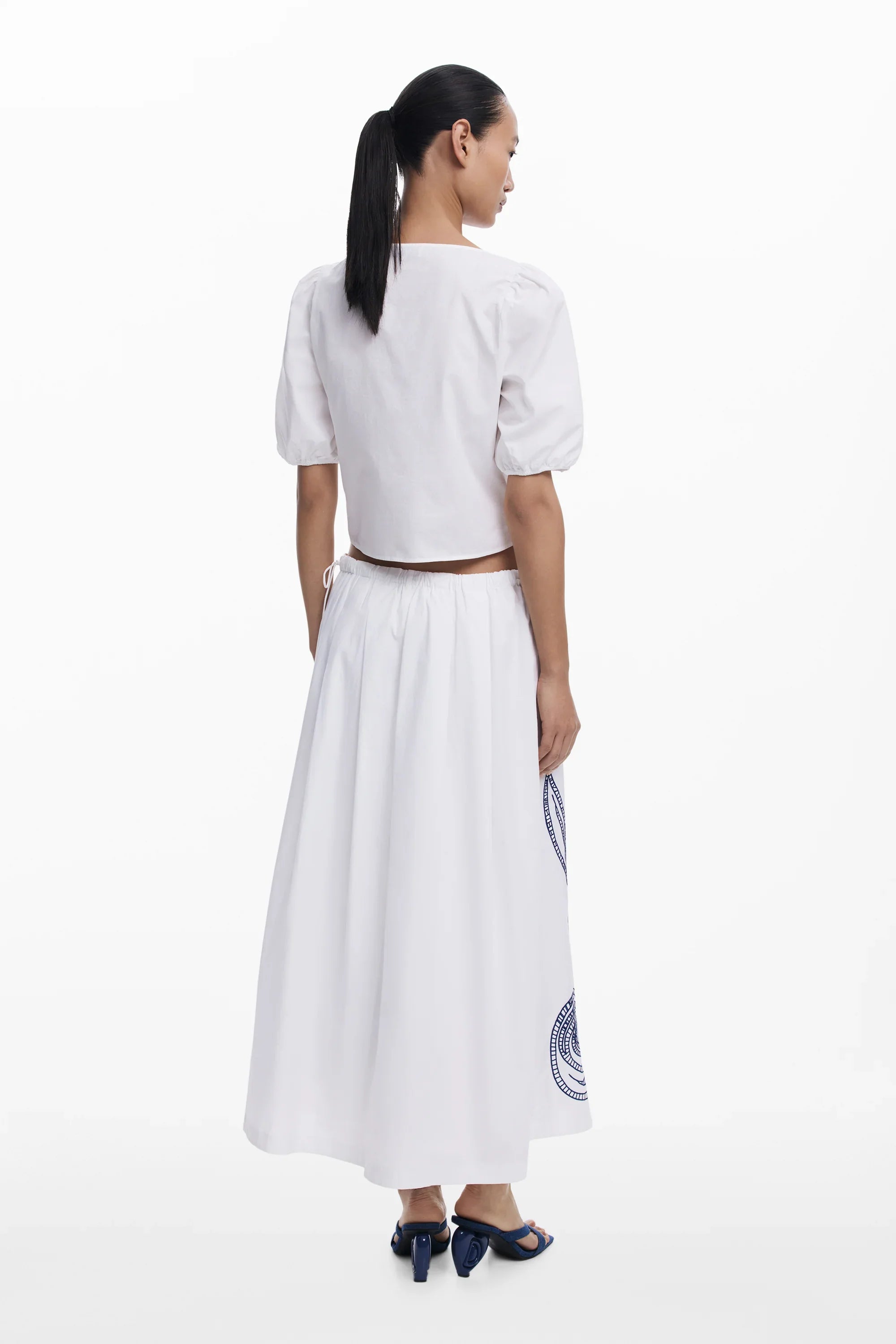 אישה עם חולצה לבנה קצרה וחצאית לבנה ארוכה עם דוגמה, מבט אחורי, צילום קטלוג CHOZEN