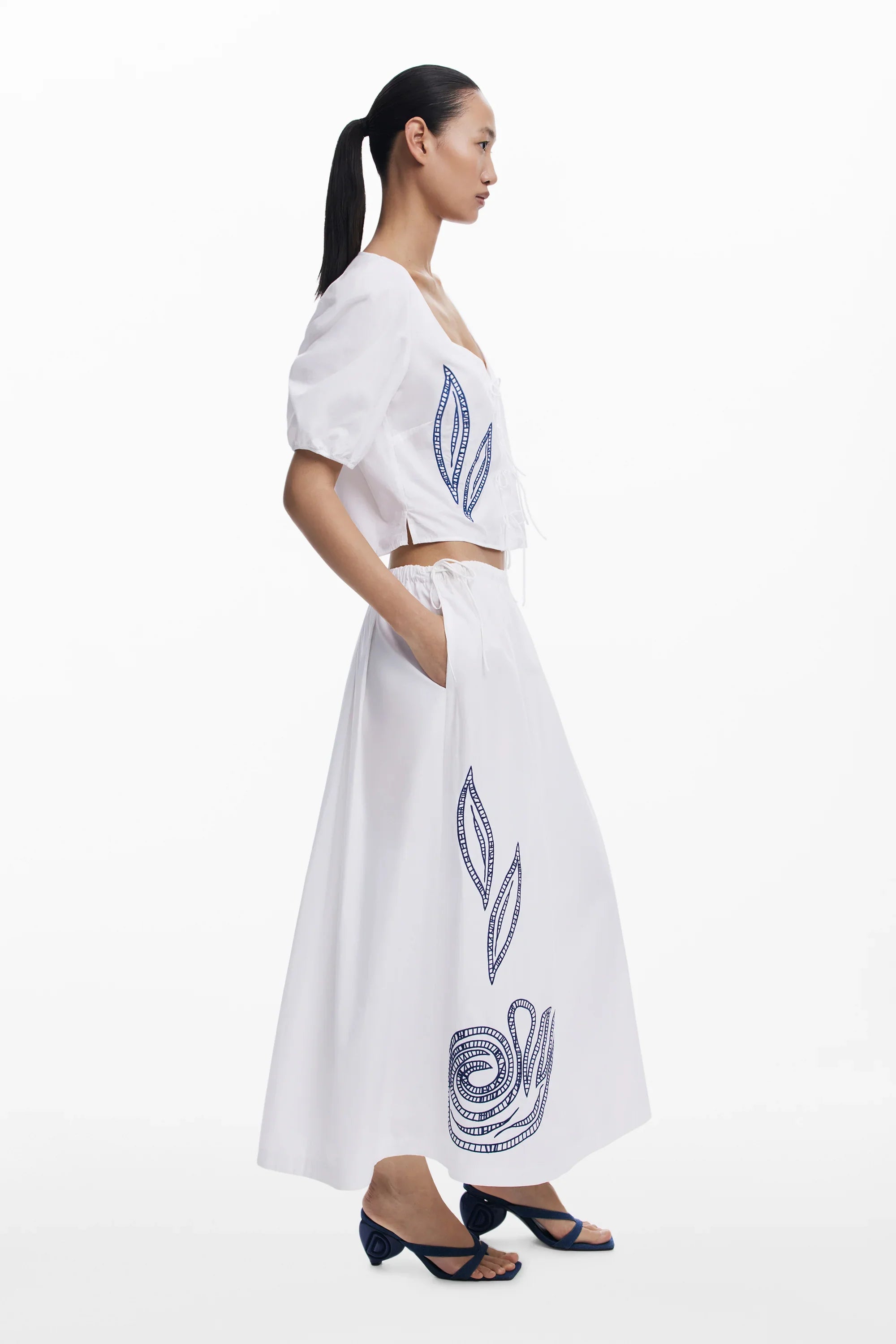 דוגמנית לובשת חצאית וטופ לבנים עם רקמה כחולה, אופנת נשים CHOZEN, טרנדי ואלגנטי