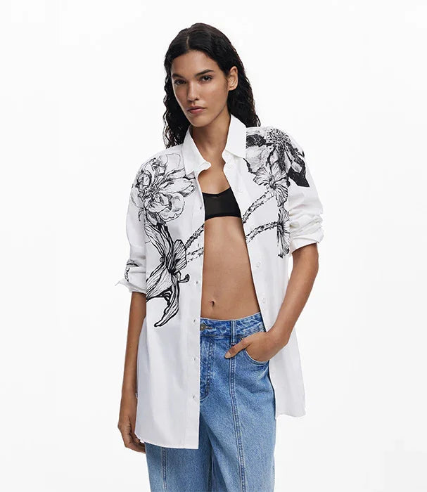 אישה לובשת חולצת כותנה לבנה עם הדפס פרחים שחור, ג'ינס כחול וטופ שחור מבית CHOZEN