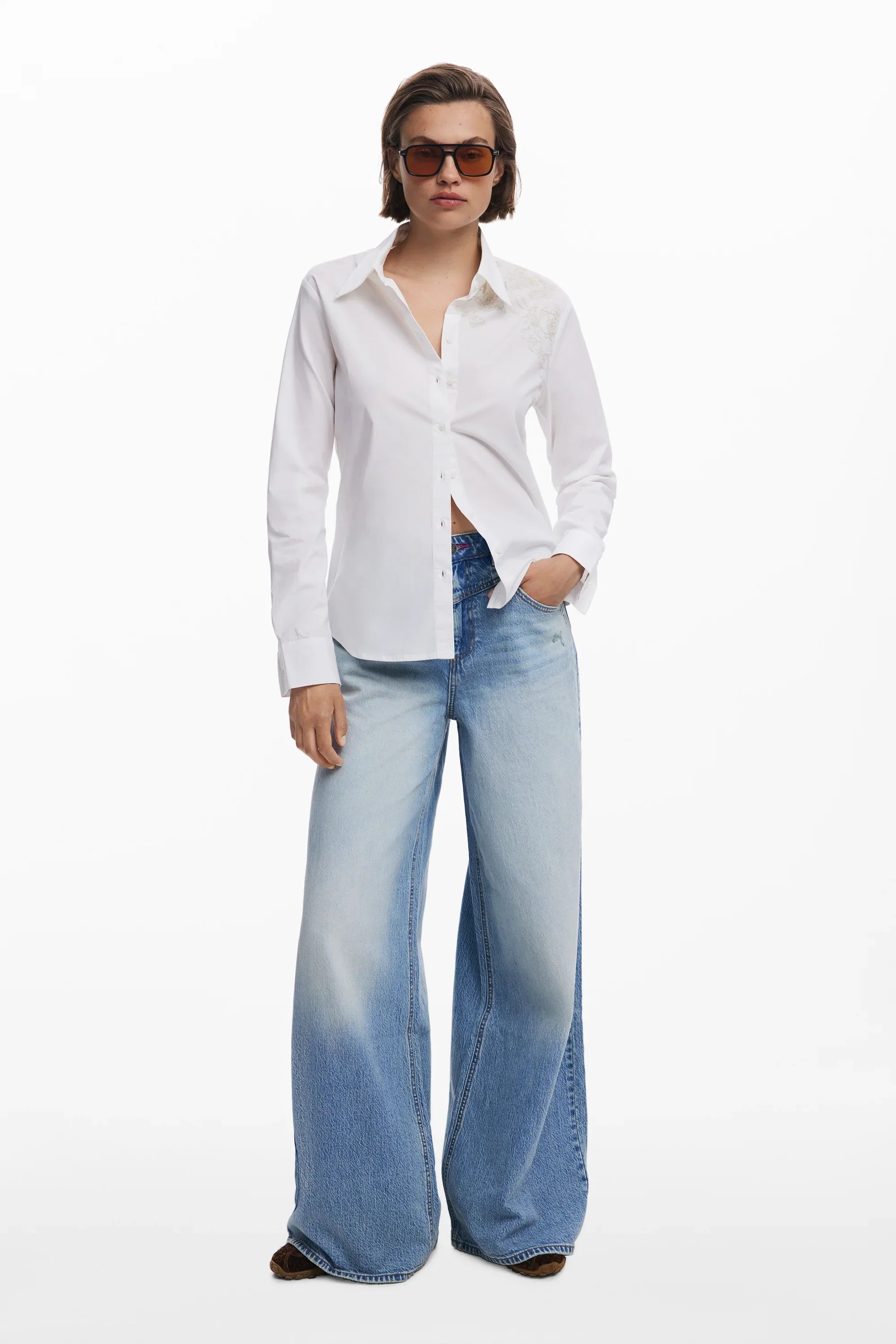 אישה עם חולצה לבנה מכופתרת, ג׳ינס כחול רחב ומשקפי שמש, אופנה CHOZEN אלפא