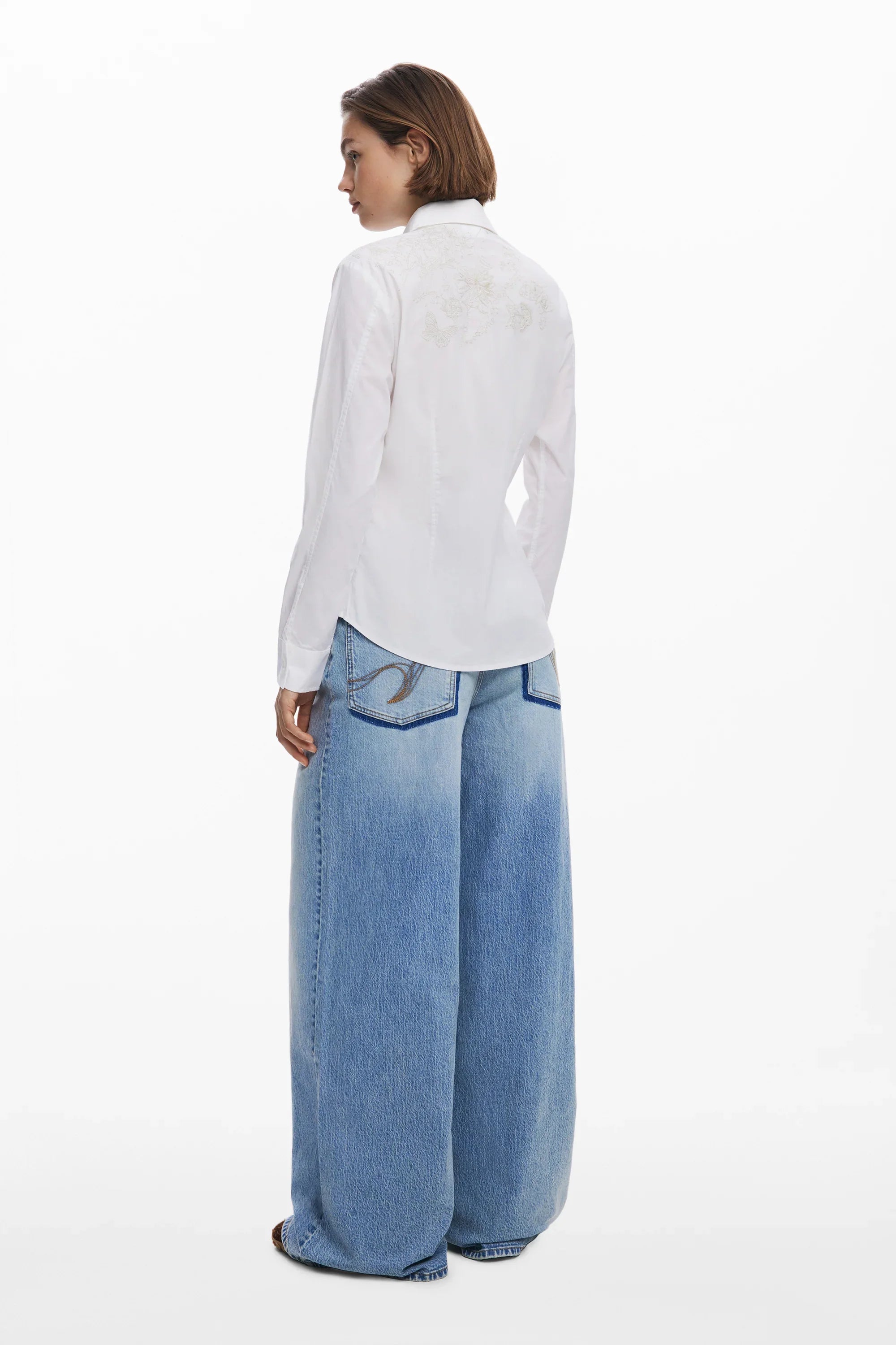 דוגמנית עם חולצה לבנה ארוכה ומכנסי ג'ינס רחבים, אופנת CHOZEN, צילום גב לאתר