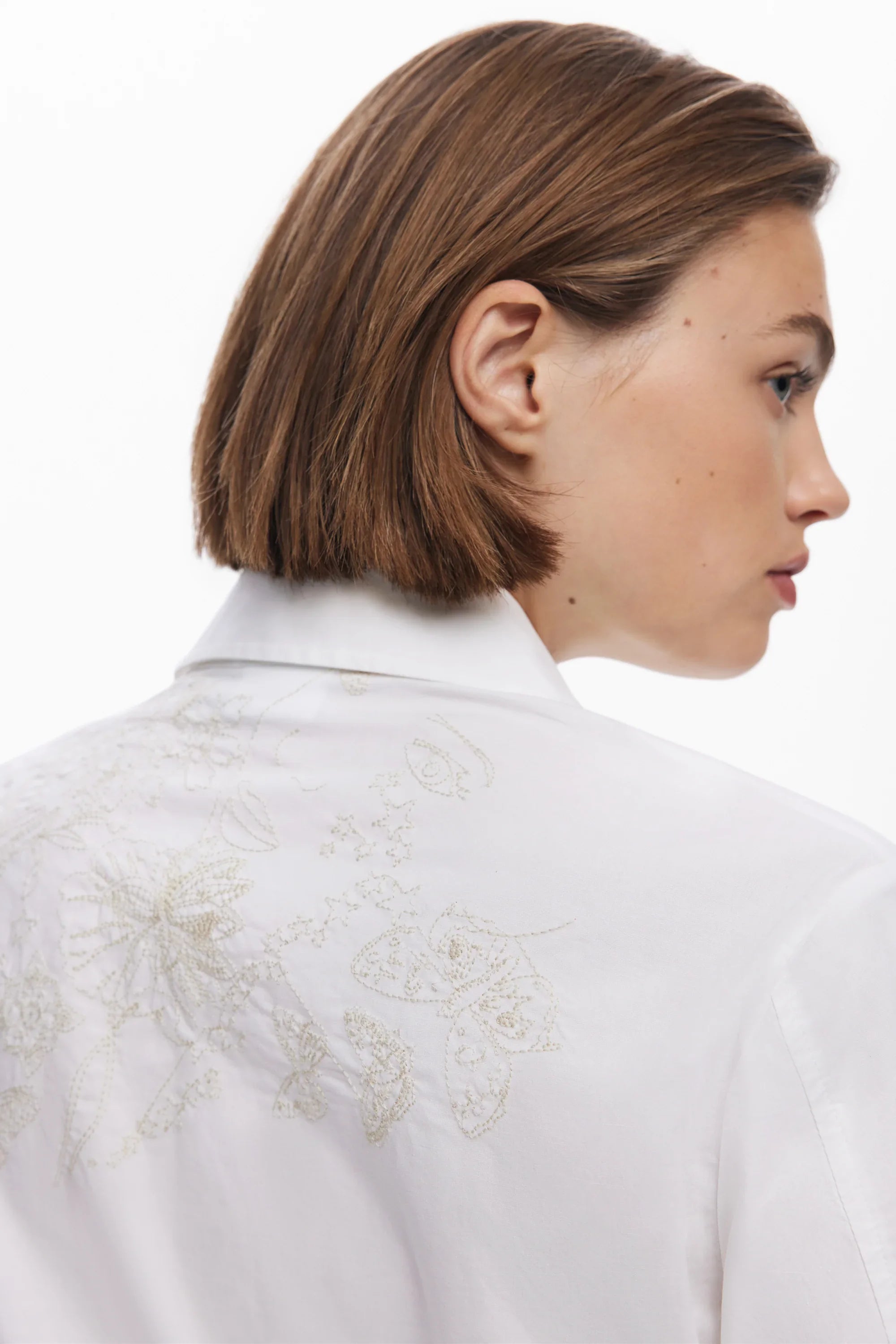 דוגמנית עם שיער חום קצר לובשת חולצה לבנה עם רקמת פרחים ופרפרים, CHOZEN אופנה מובחרת