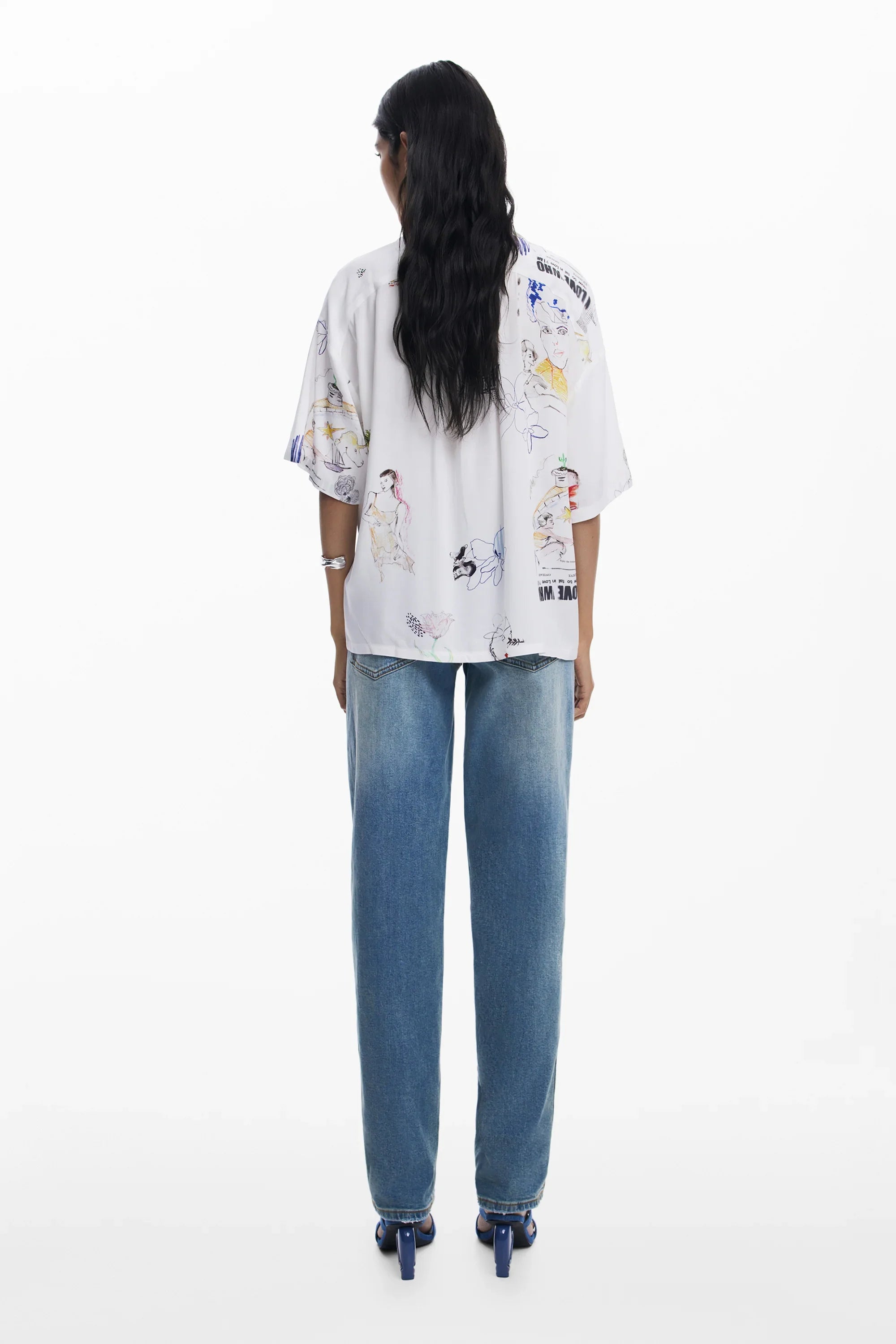 אישה עם חולצה לבנה עם הדפסי איורים צבעוניים ומכנסי ג'ינס כחולים עומדת על רקע לבן, אופנה CHOZEN