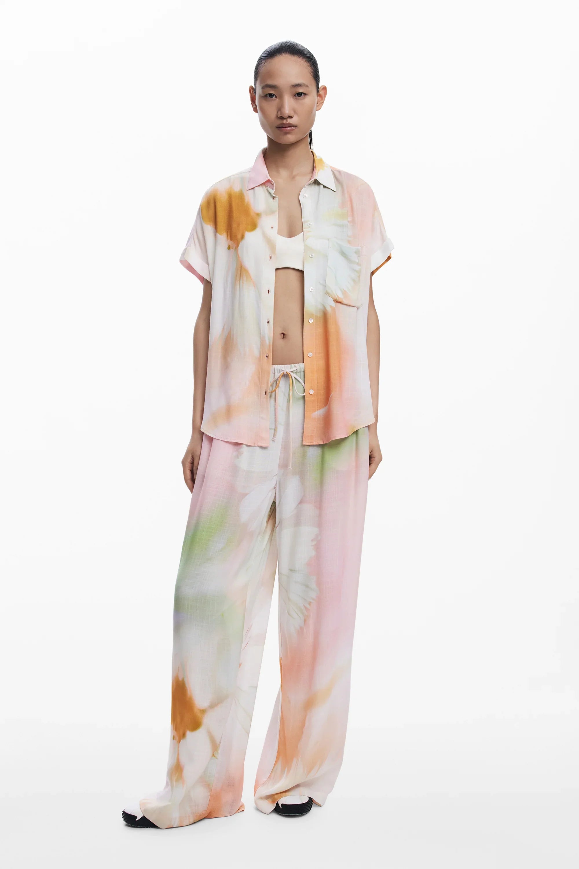 דוגמנית לובשת חליפת נשים במראה פרחוני צבעוני של CHOZEN, חולצה מכופתרת ומכנסיים רחבים, רקע לבן