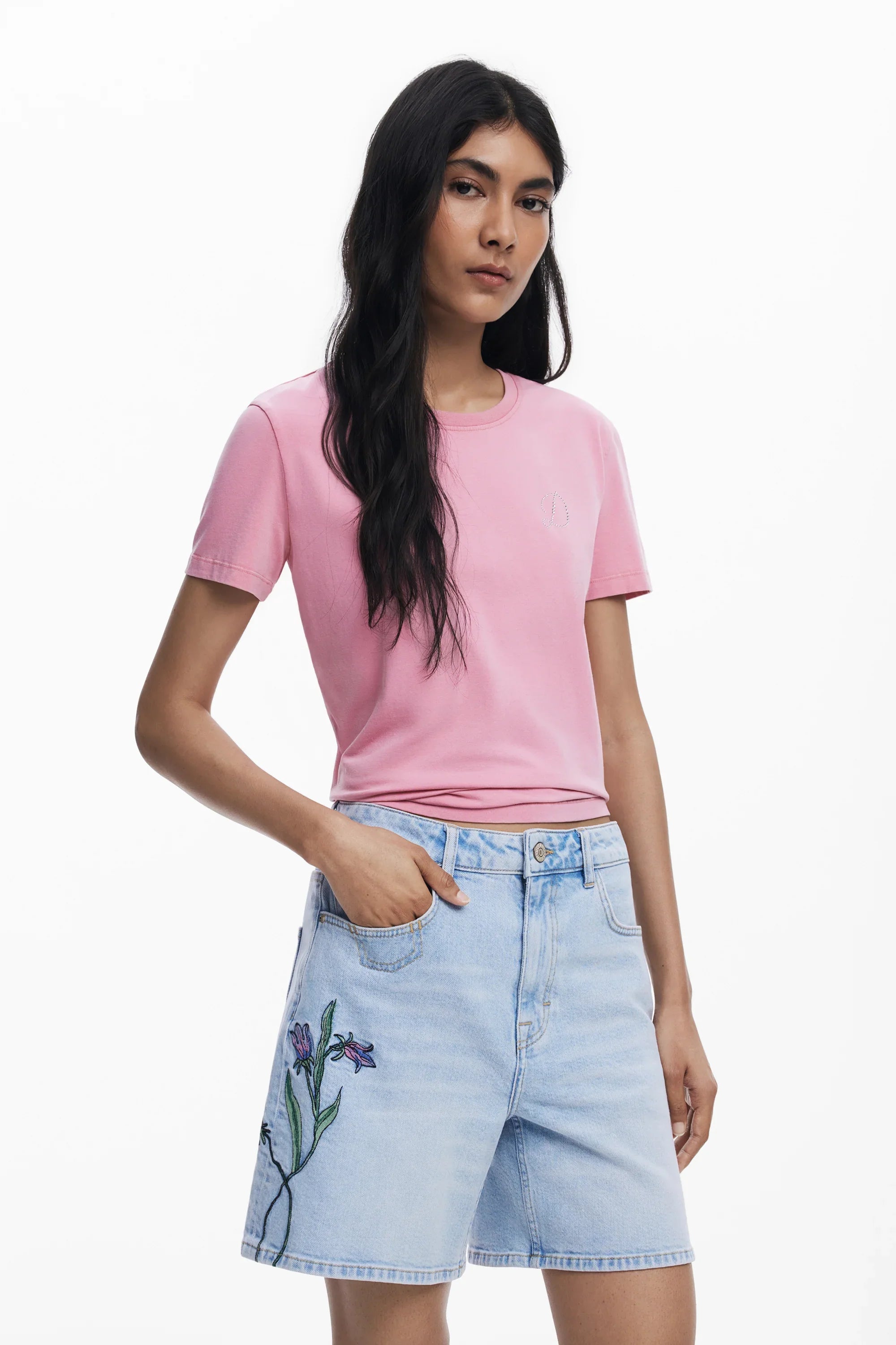 אישה בשיער שחור לובשת חולצה ורודה ומכנסי ג'ינס קצרים עם רקמה של פרחים, אופנת CHOZEN