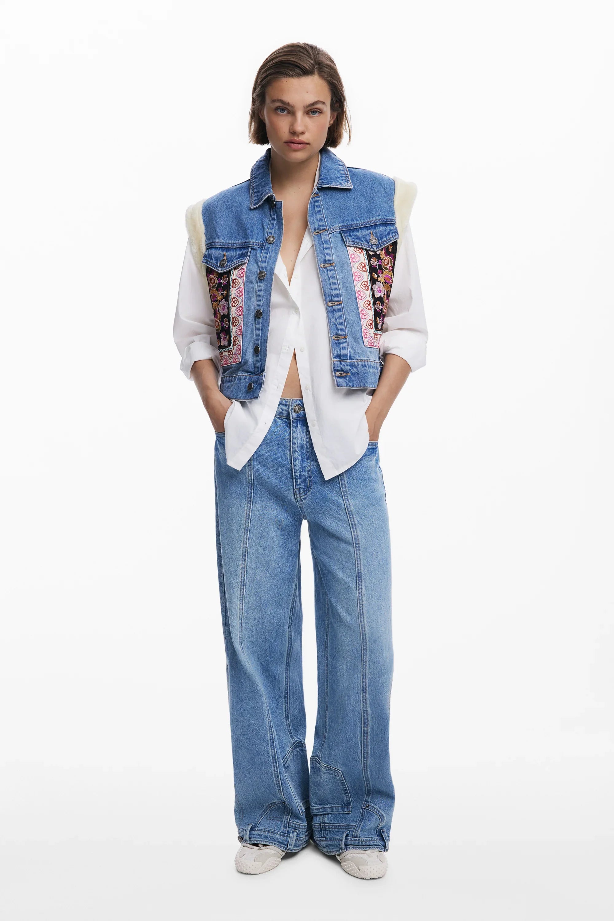 דוגמנית לובשת וסט ג'ינס עם דוגמה פרחונית, חולצה לבנה ומכנסי ג'ינס רחבים CHOZEN