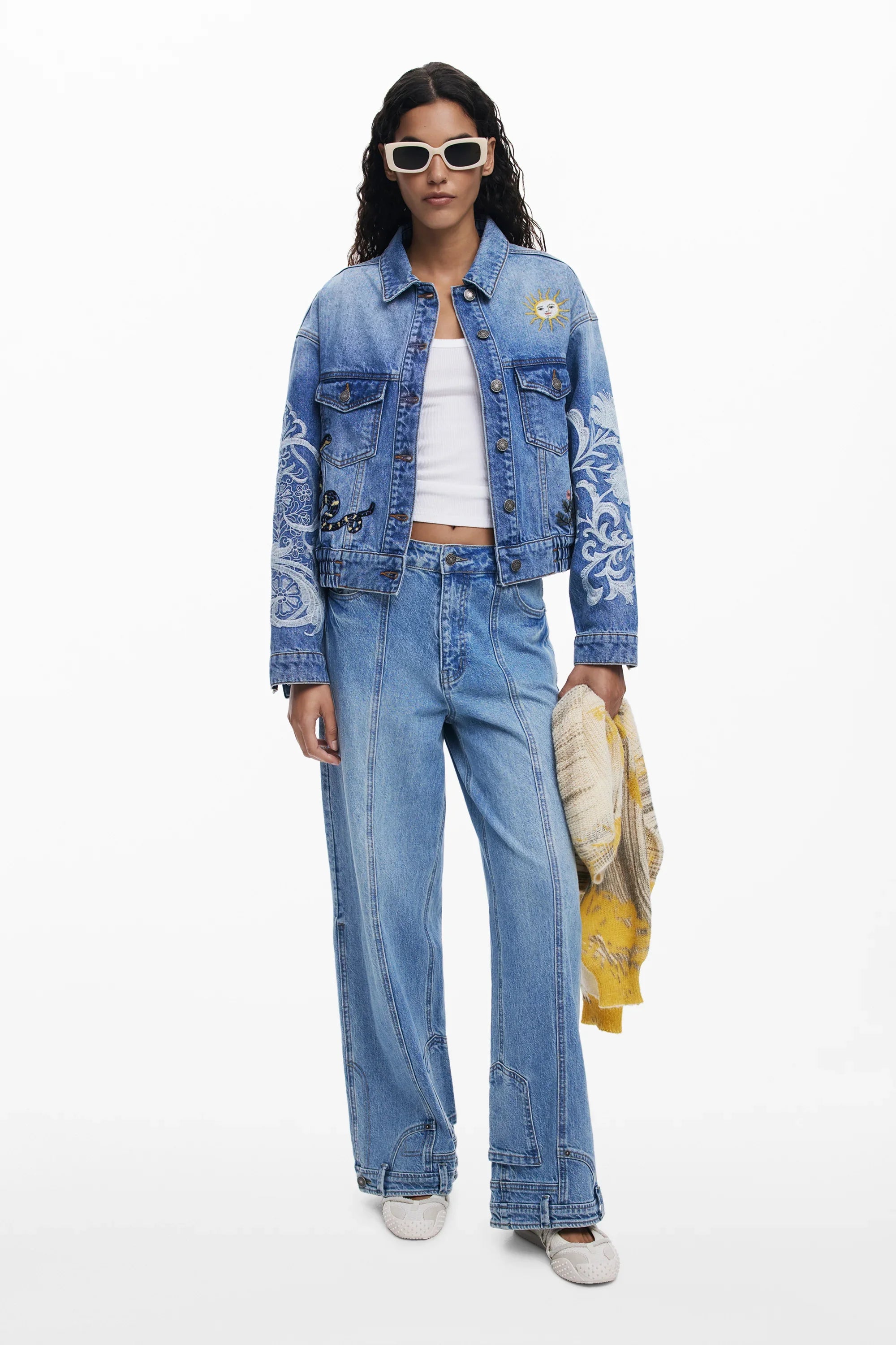 דוגמנית עם משקפי שמש, לובשת ג'קט ג'ינס ופרטי רקמה, מכנסי ג'ינס, טופ לבן – אופנה CHOZEN