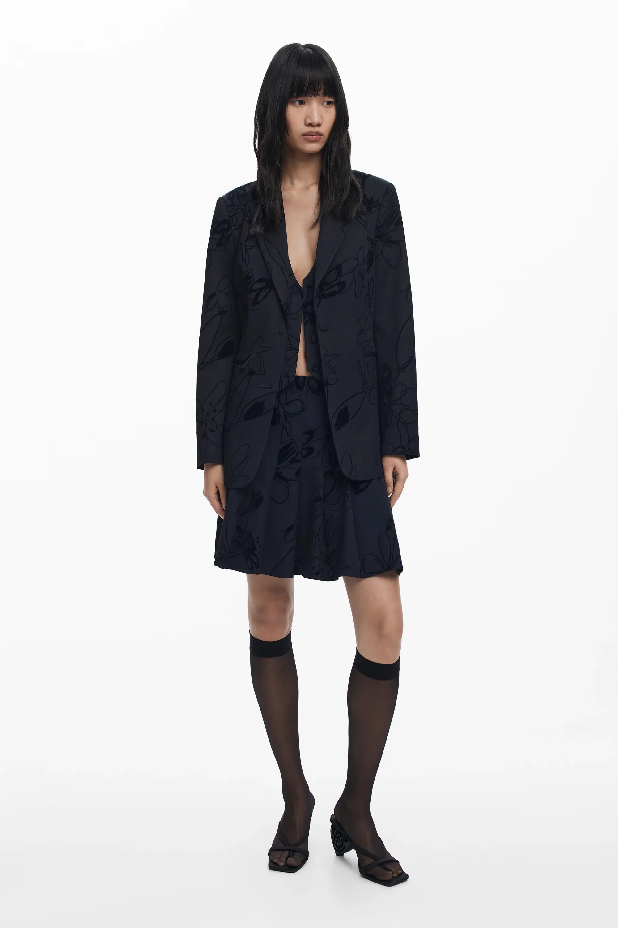 דוגמנית לובשת חליפה שחורה עם דוגמת פרחים, חצאית, גרביים שקופים ונעליים, אופנת נשים CHOZEN