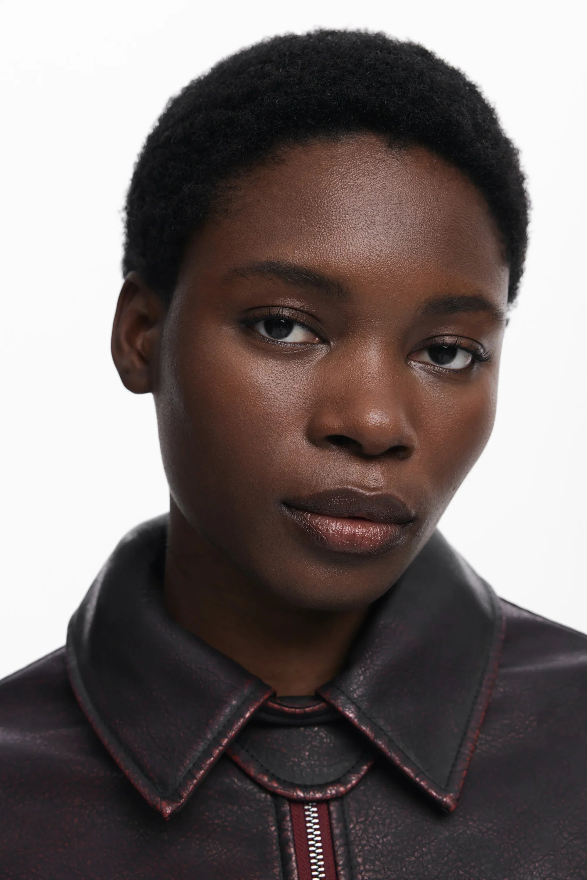 תקריב פנים של אישה עם שיער קצר, לובשת ז'קט עור בורדו, רקע לבן, CHOZEN מותגים מובילים