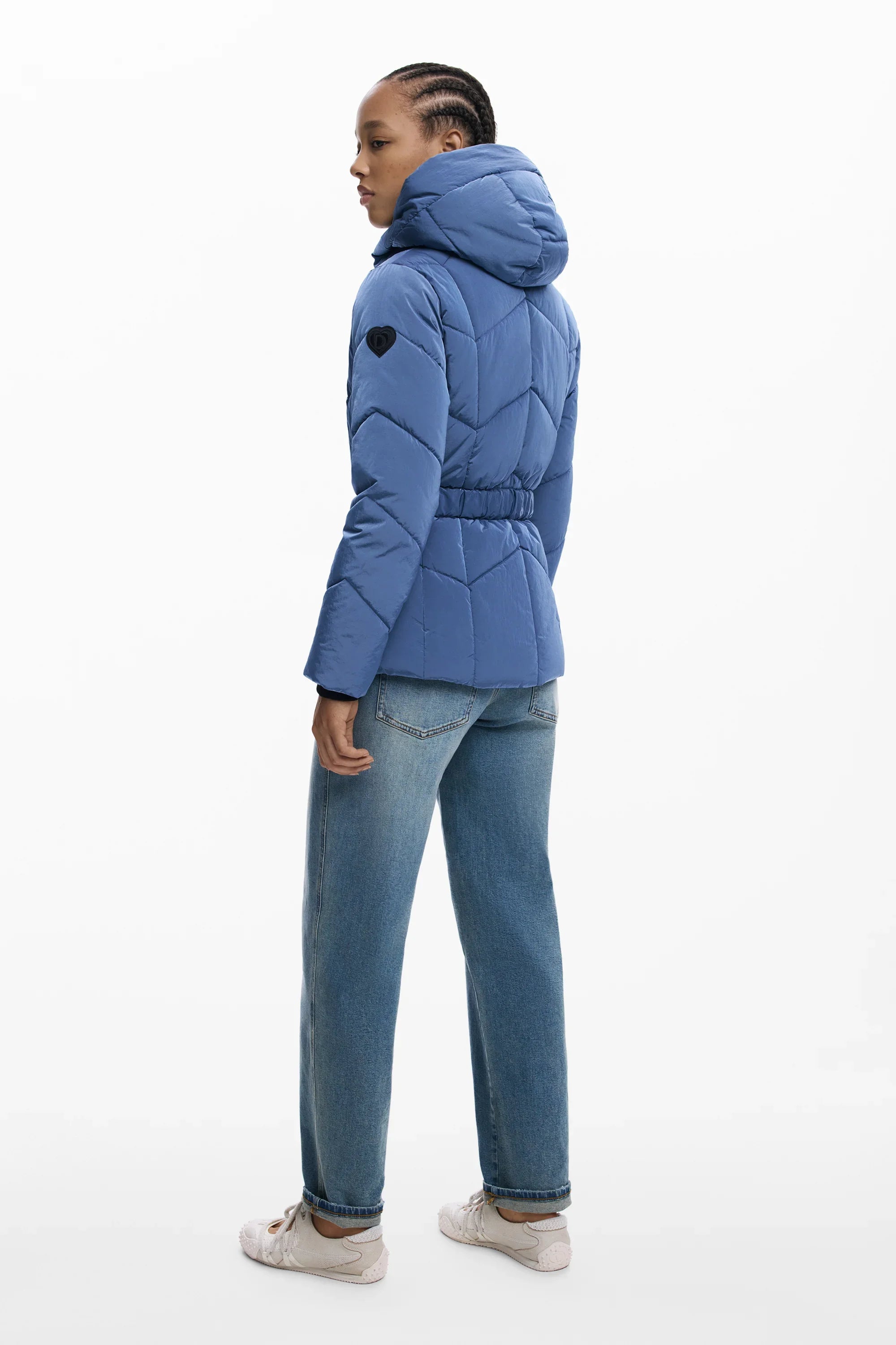 אישה לובשת מעיל פוך כחול עם קפוצ'ון, ג'ינס ונעלי ספורט רקע לבן, אופנה CHOZEN