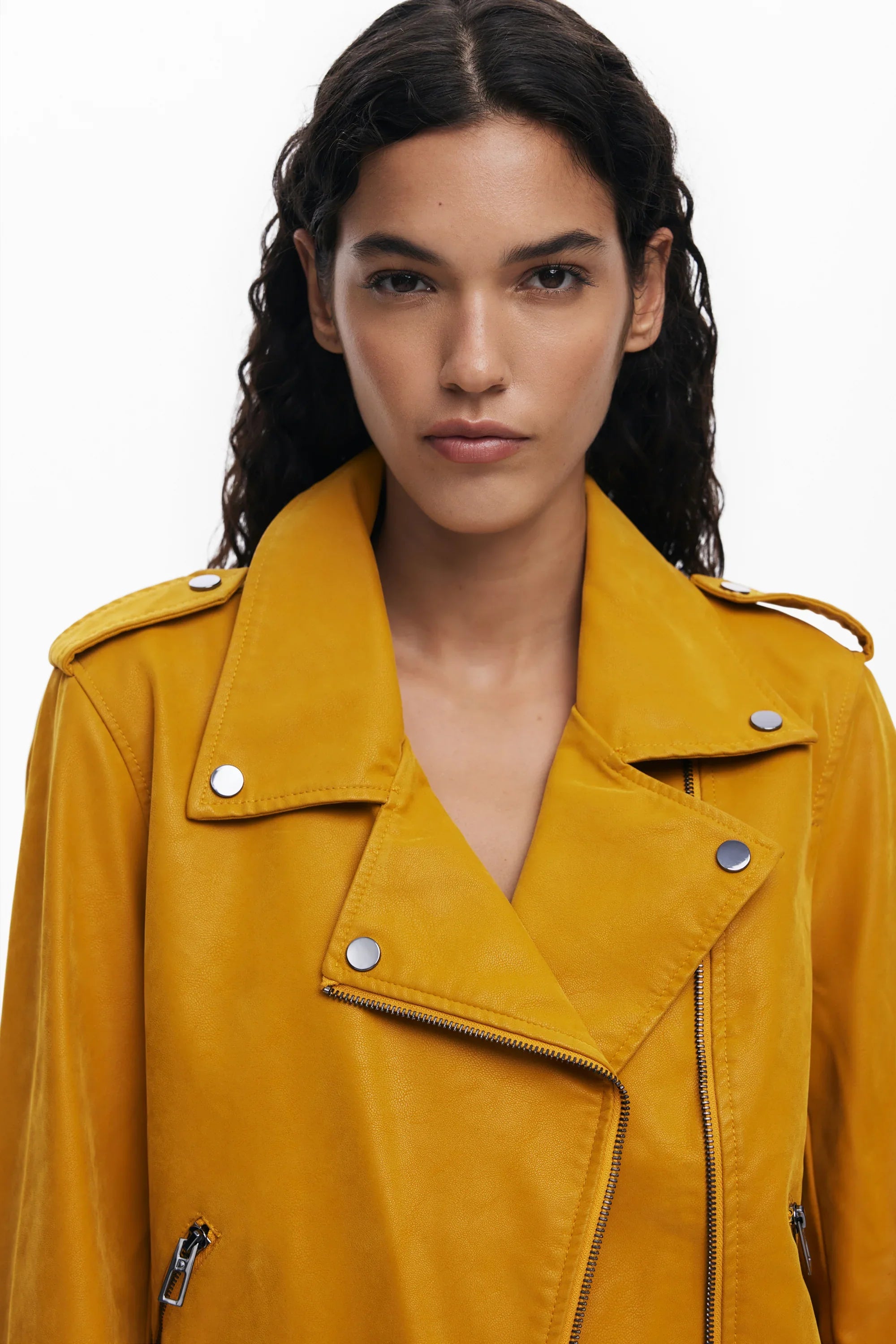 אישה עם שיער מתולתל לובשת מעיל עור אופנתי בצבע חרדל, צילום סטודיו ל-CHOZEN