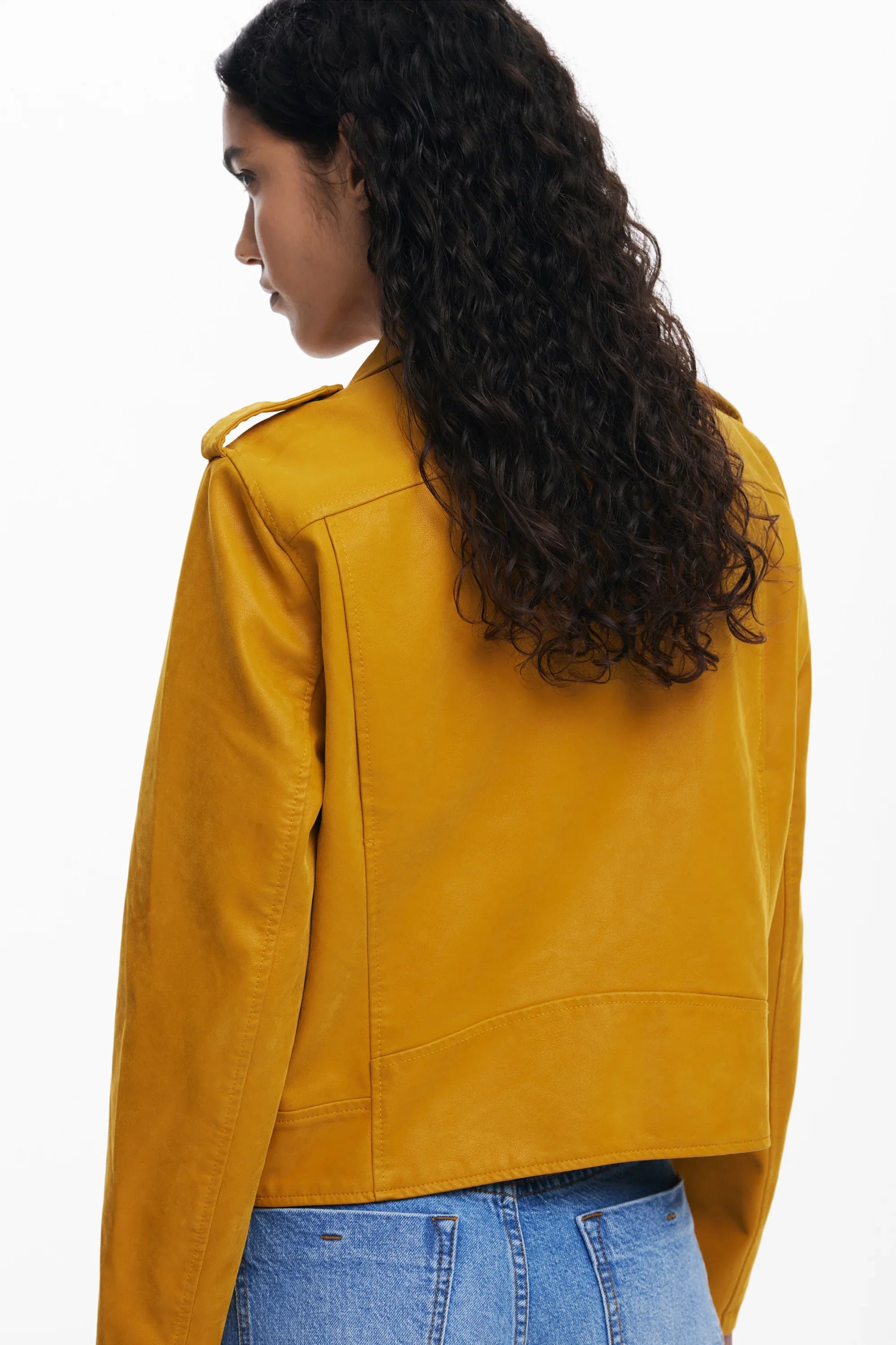 אישה עם שיער מתולתל לובשת ז'קט עור חרדל אופנתי ומכנסי ג'ינס, צילום גב, קולקציית CHOZEN