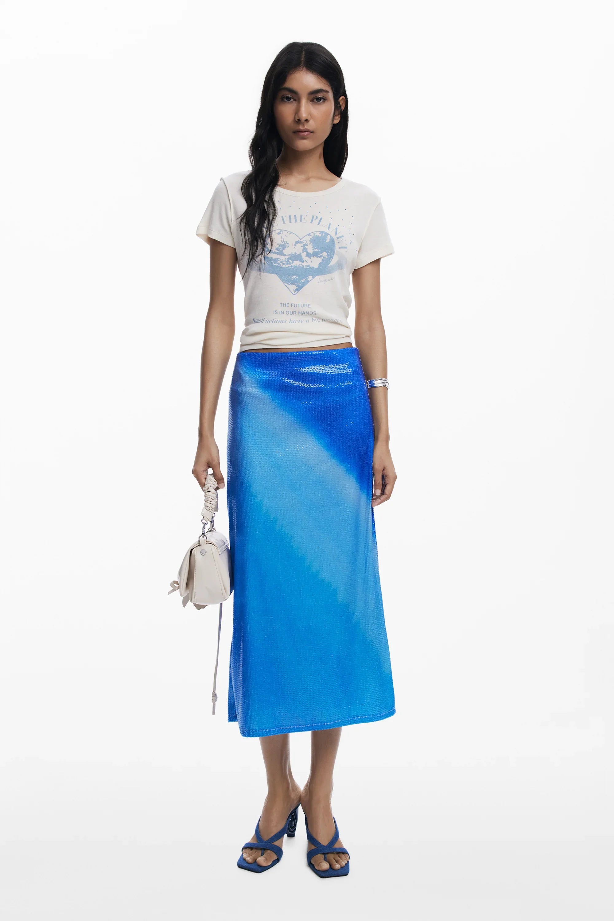 אופנת קיץ לנשים של CHOZEN, דוגמנית עם חולצת טי לבנה וחצאית כחולה מבריקה, נעלי עקב כחולות ותיק בהיר