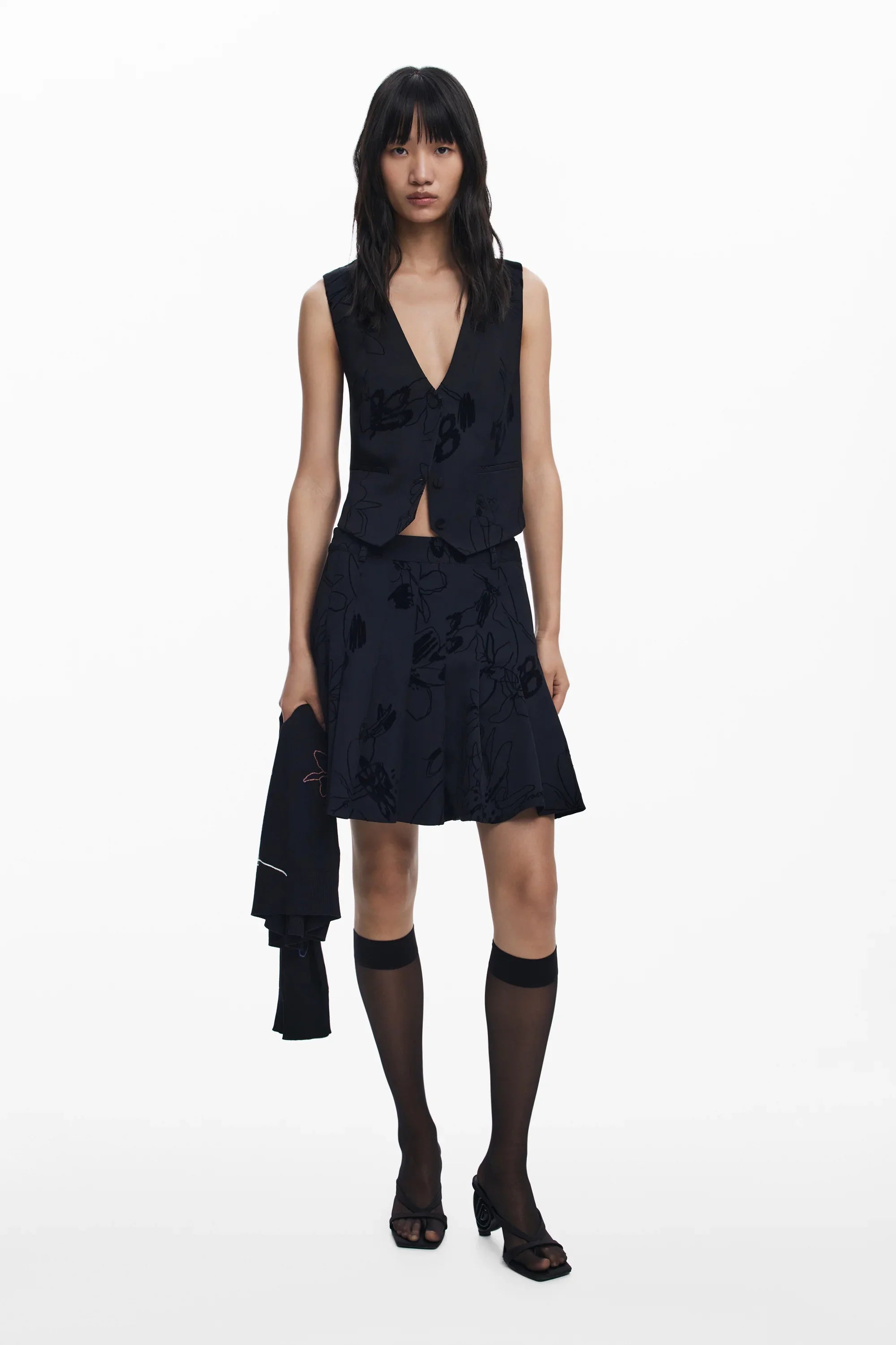 דוגמנית לובשת חליפת שתי חלקים שחורה עם דוגמת פרחים, גרביים שקופות ועקבים. CHOZEN מותגים מובילים