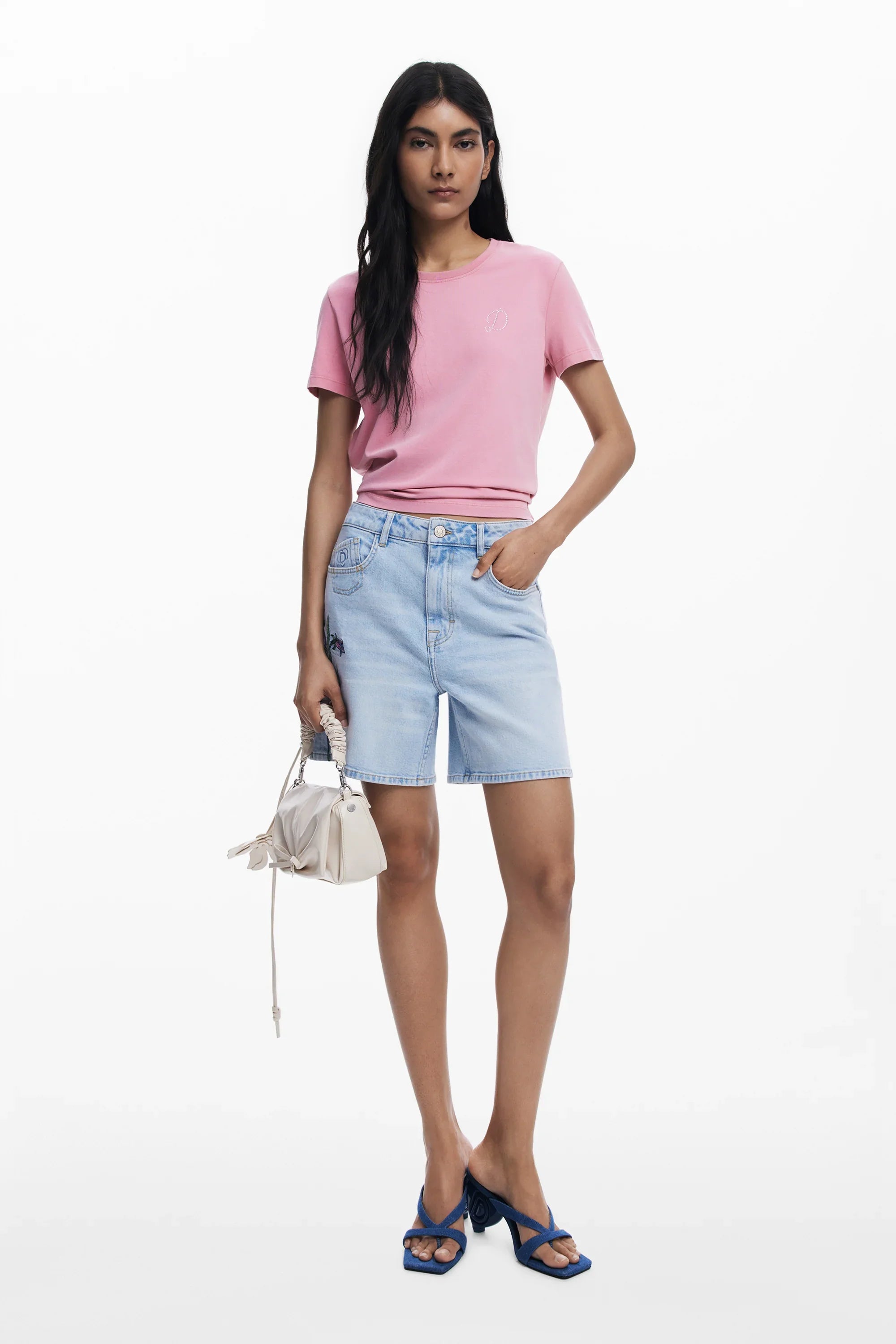 אופנת נשים CHOZEN: דוגמנית עם חולצת טי ורודה, מכנס ג'ינס קצר, תיק לבן וסנדלים כחולים