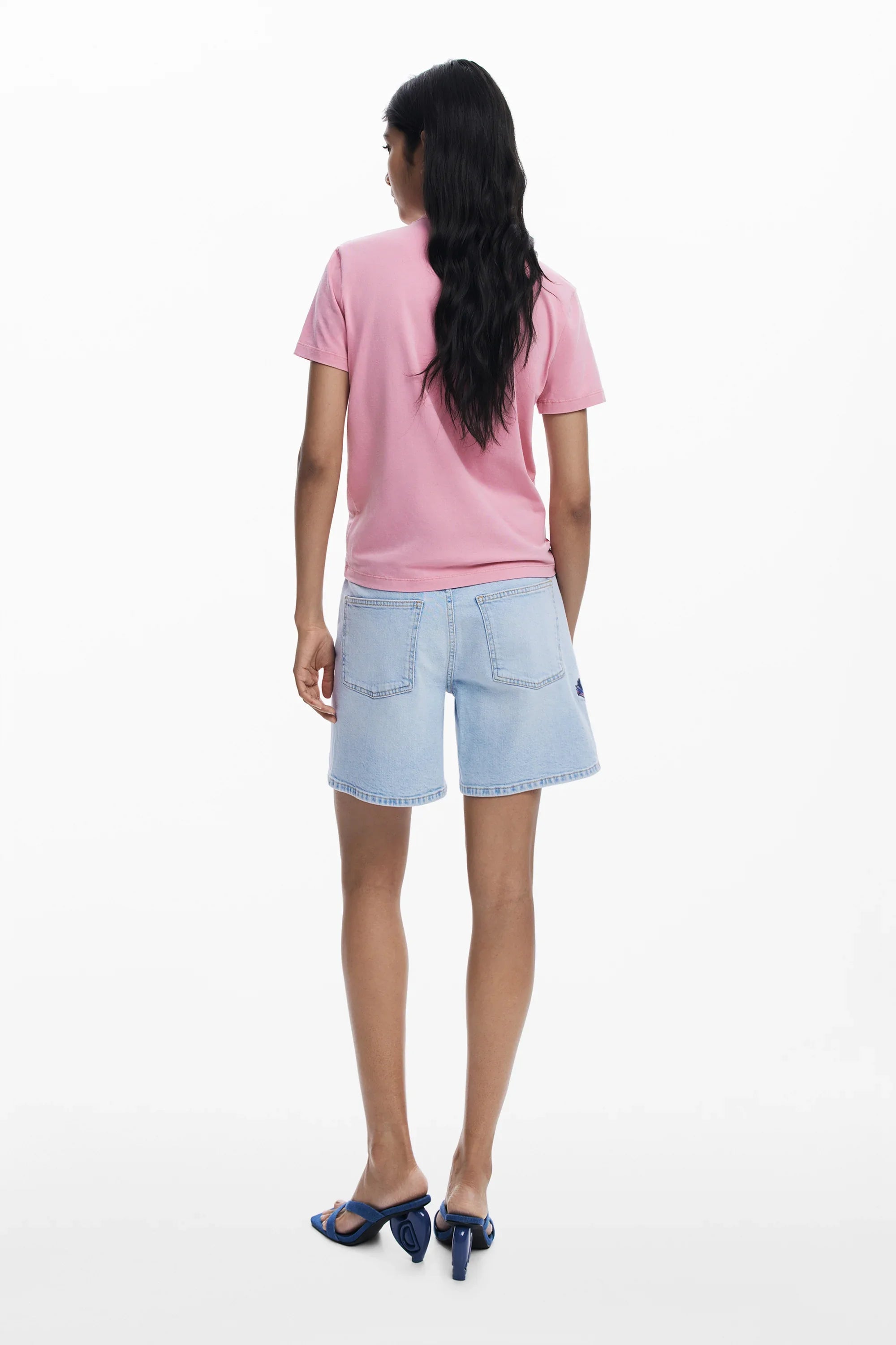 אישה עם שיער ארוך לובשת טי שירט ורודה, שורט ג'ינס תכלת ונעליים כחולות, צילום לאחור, CHOZEN