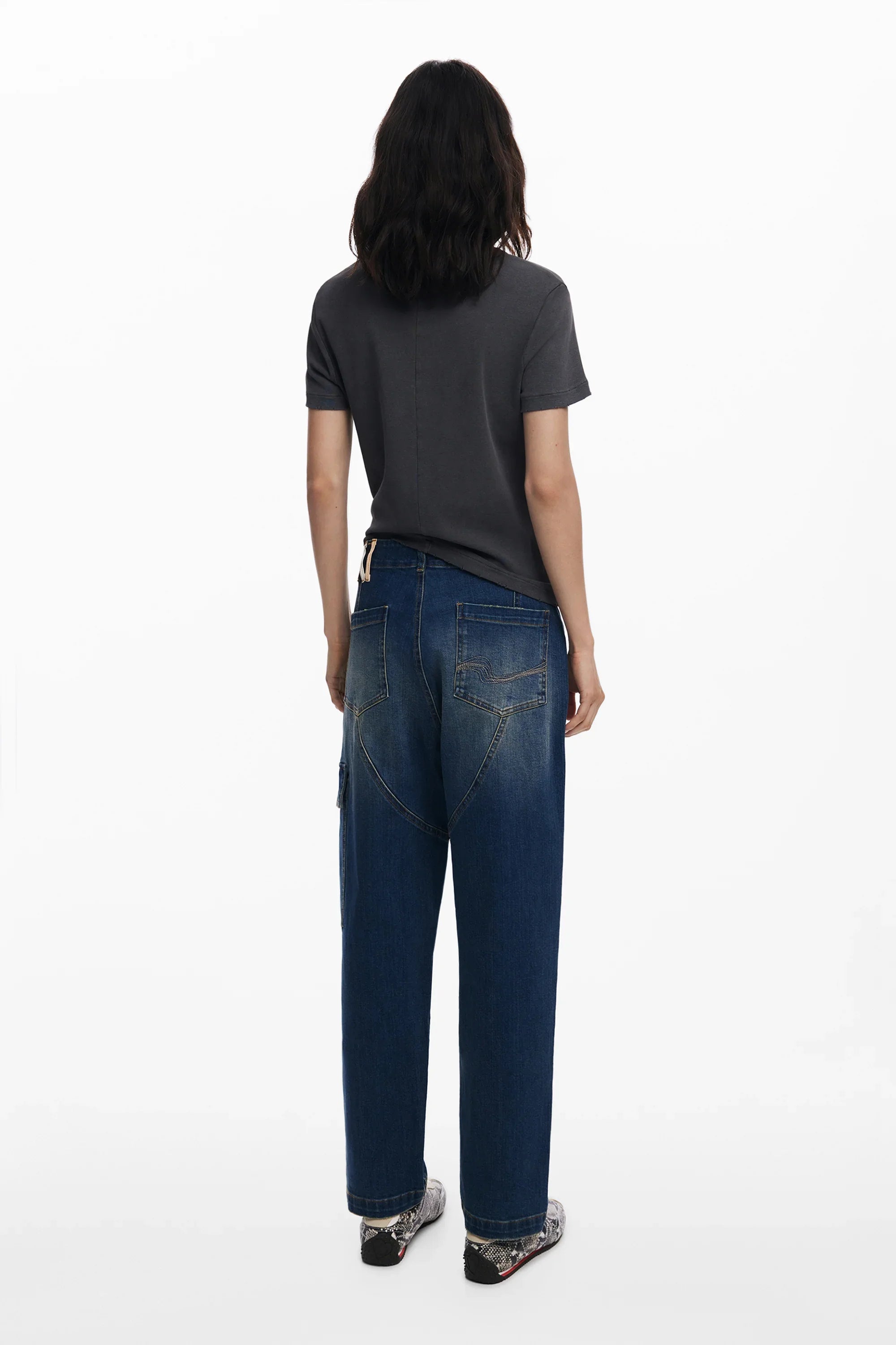 אישה עם חולצה אפורה ומכנסי ג'ינס רחבים עומדת על רקע לבן, אופנה מבית CHOZEN