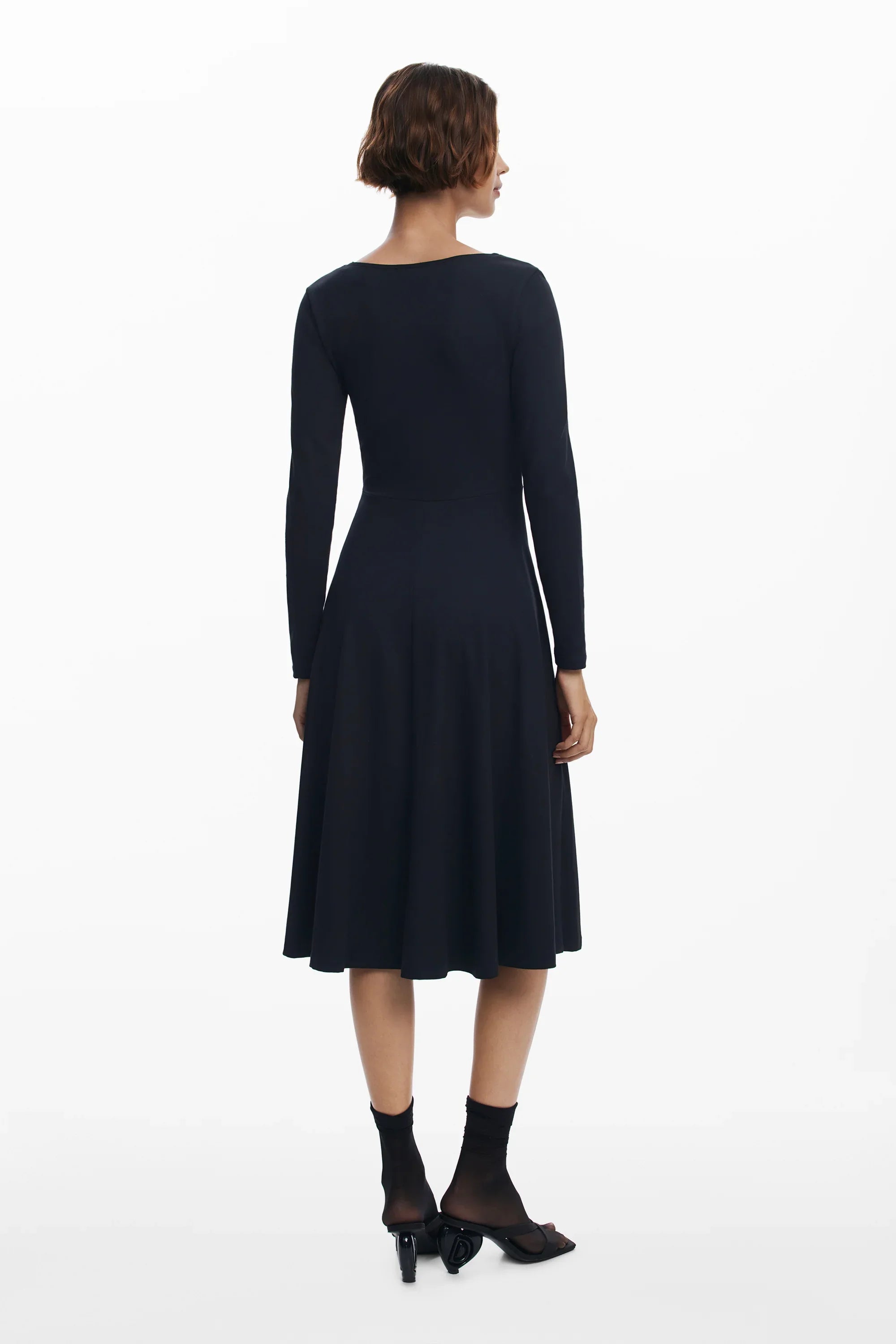 אישה עם שמלת מידי שחורה עם שרוולים ארוכים, מצולמת מאחור רקע לבן, אופנה CHOZEN