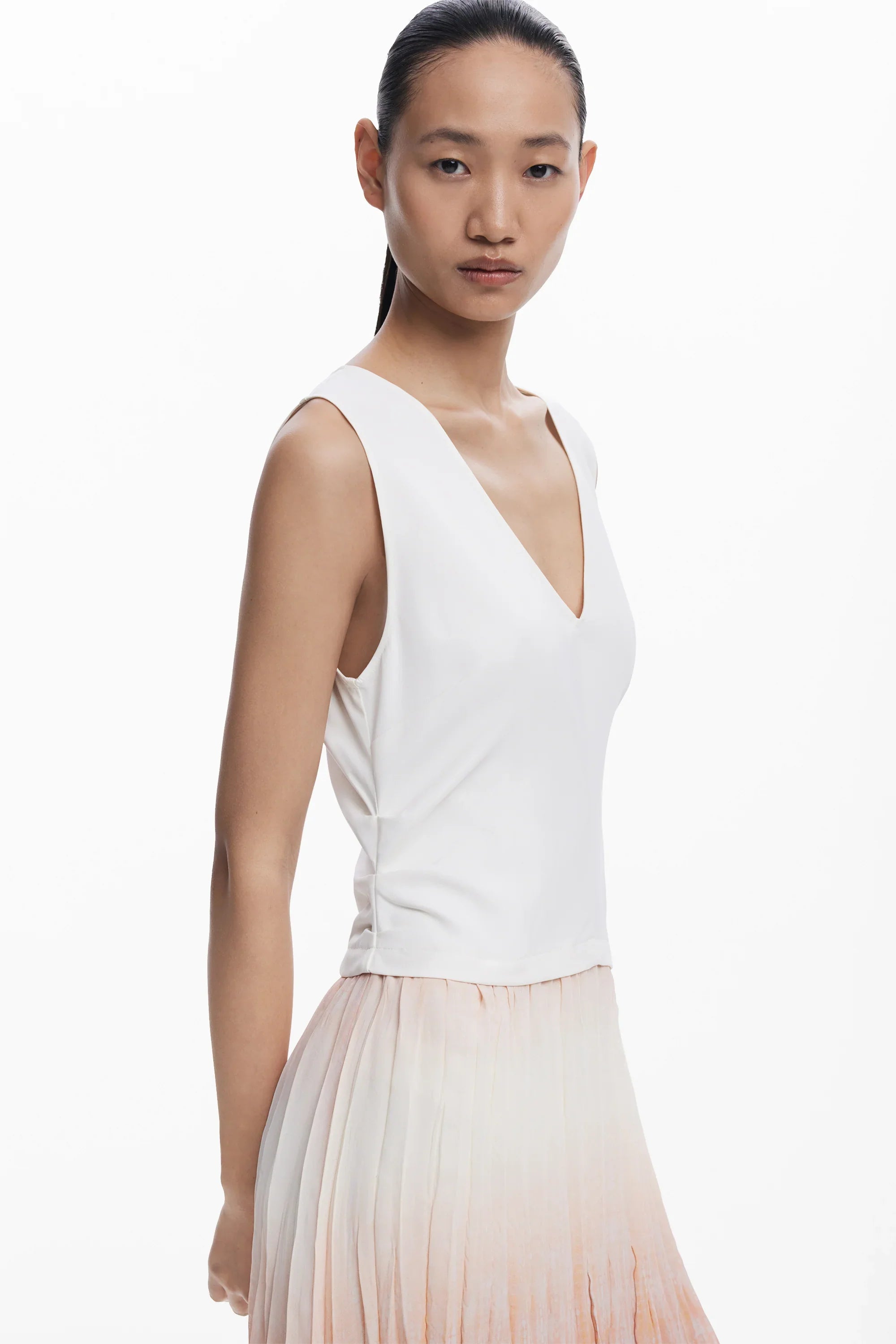 דוגמנית עם גופיית וי לבנה וחצאית פליסה בהירה, אופנה יוקרתית ב-CHOZEN