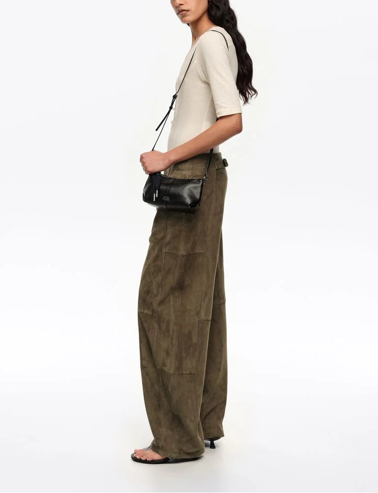 אישה לובשת חולצת בז' עם מכנסי זמש חומים רחבים, תיק קטן שחור על כתף ונעלי סנדל שחורות