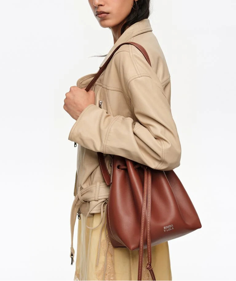 אישה עם מעיל בז' נושאת תיק כתף עור חום בעיצוב בקט סלינג אופנתי