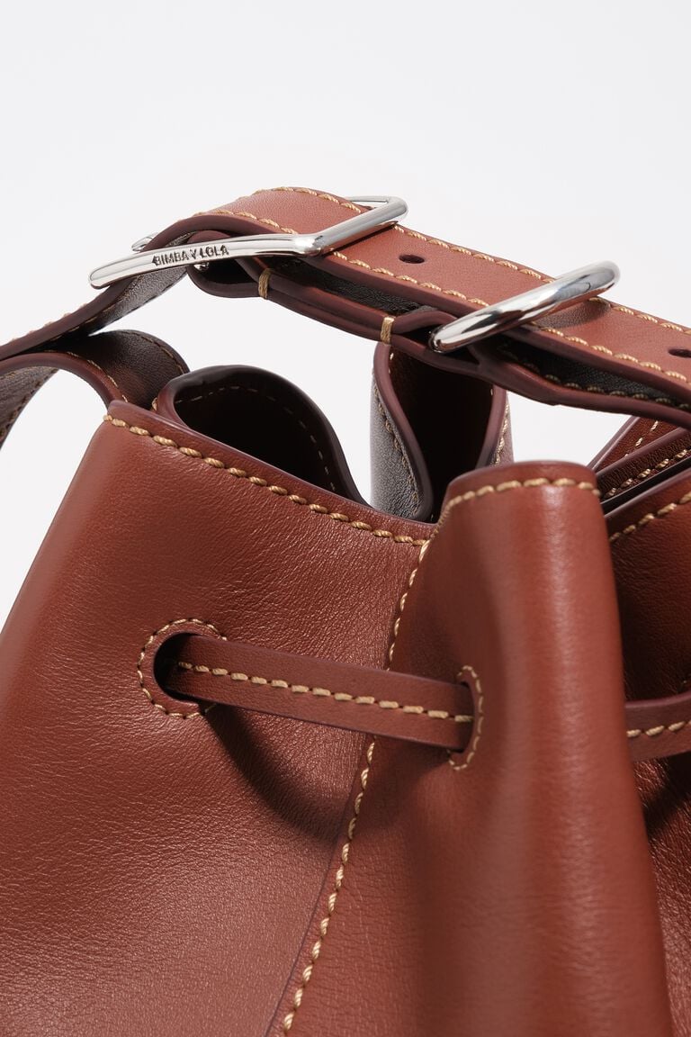 תקריב של תיק עור חום עם תפרים בהירים, סוגר אבזם מתכת ועיצוב איכותי