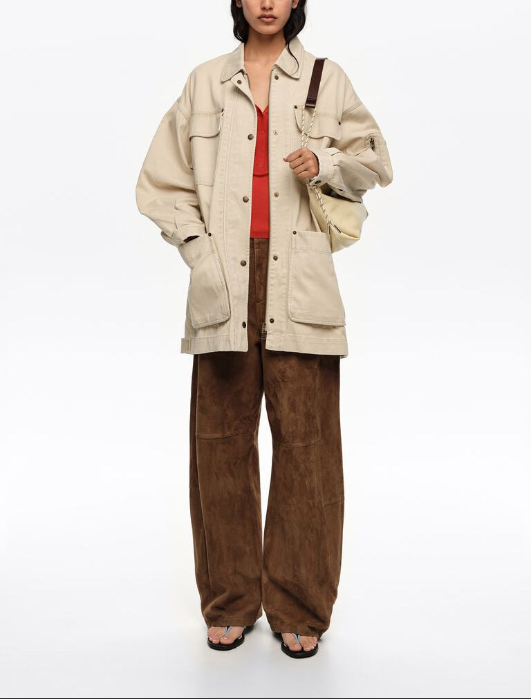 אישה לובשת ז'קט בגוון בז', מכנסיים חומים רחבים, גופיה אדומה ותיק כתף בהיר