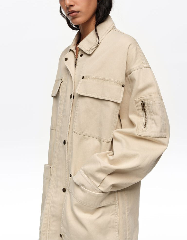 אישה לובשת ג'קט בגוון בז', כיסים קדמיים גדולים ועיצוב קז'ואל מודרני