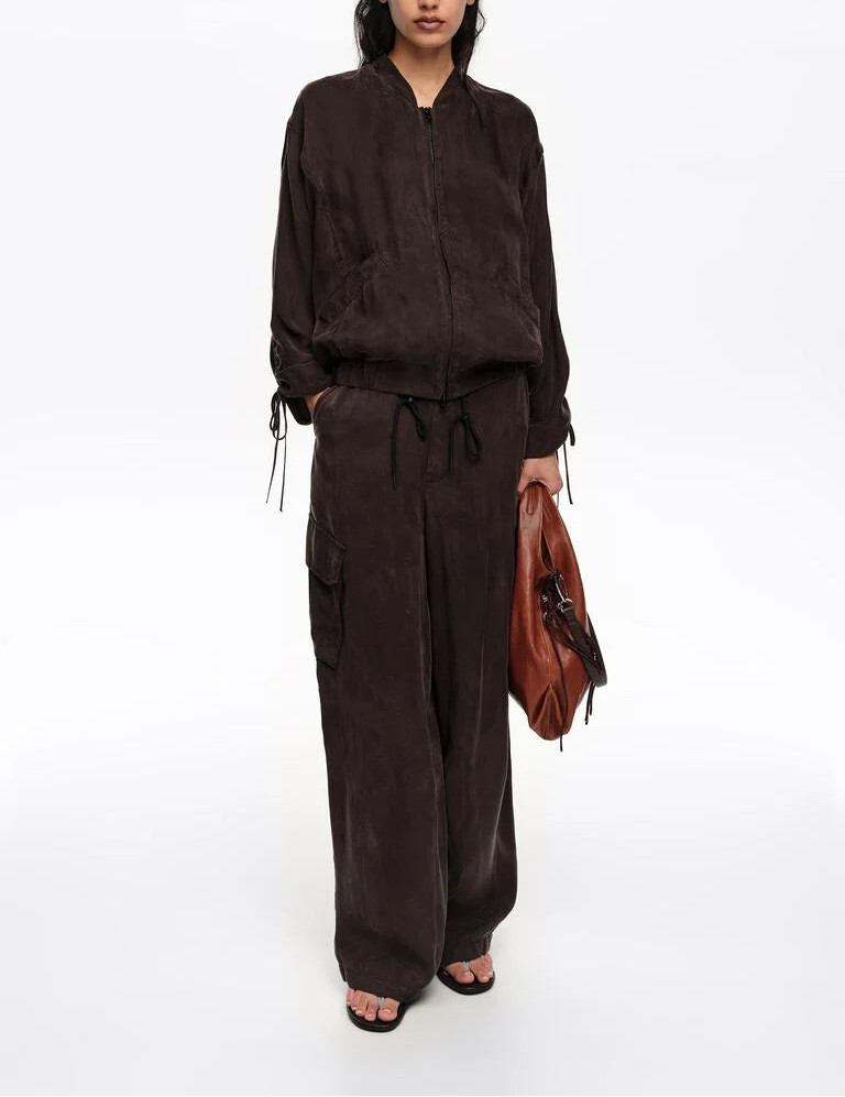 אישה לובשת חליפת טרנינג שחורה עם מכנסי כיסים רחבים, מחזיקה תיק חום