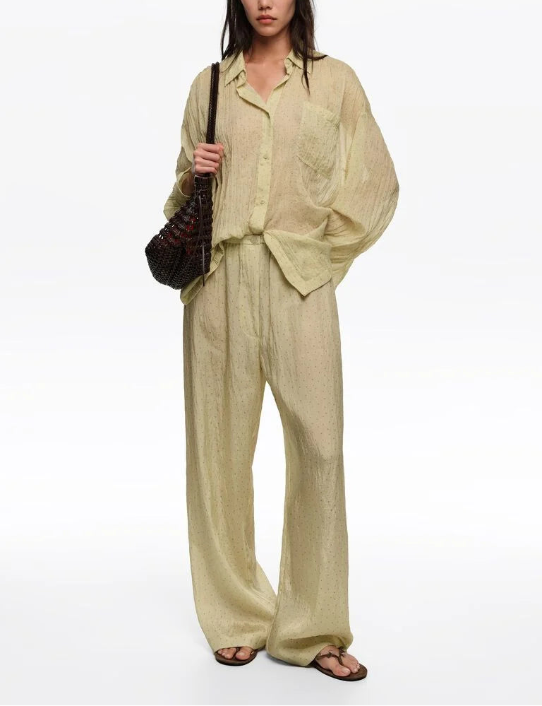 אישה לובשת סט מכנסיים וחולצה רחבים מבד בהיר שקוף, תיק צד, כפכפים