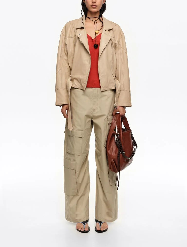 אישה לובשת מעיל עור בז', גופיה אדומה, מכנסי קארגו בז', תיק חום וסנדלים שחורים